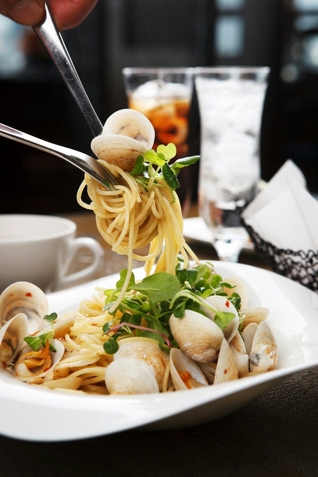 En närbild av lite spaghetti alle vongole som vrids på en gaffel från en vit maträtt.  Det finns färska örter, musslor och en lätt sås på en pastabädd.