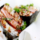 Closeup of a slice of grilled spam on top of a block of rice wrapped together with nori dried seaweed 