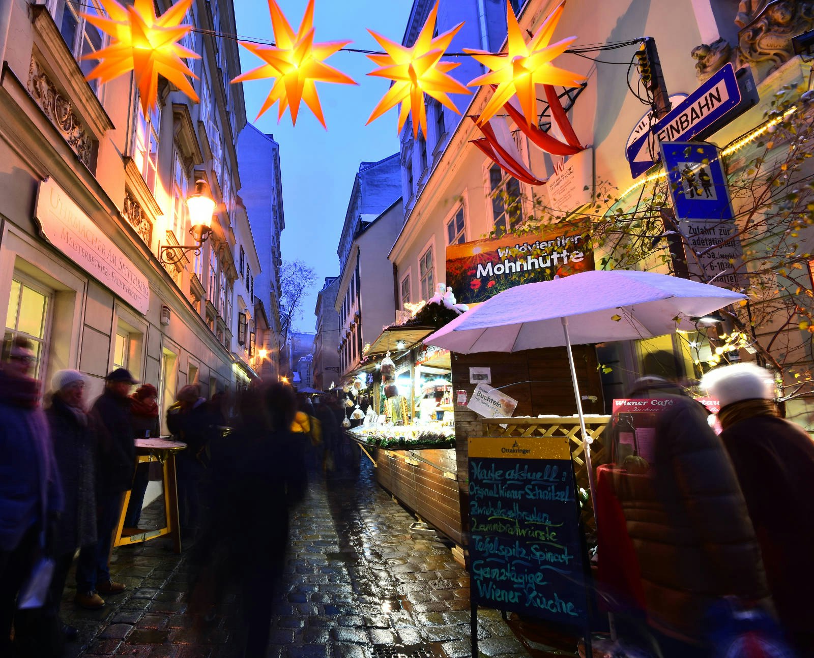 Stalls squeezed into narrow cobblestone streets. It's nearly dark and has been raining and there are star-shaped lights hanging overhead.