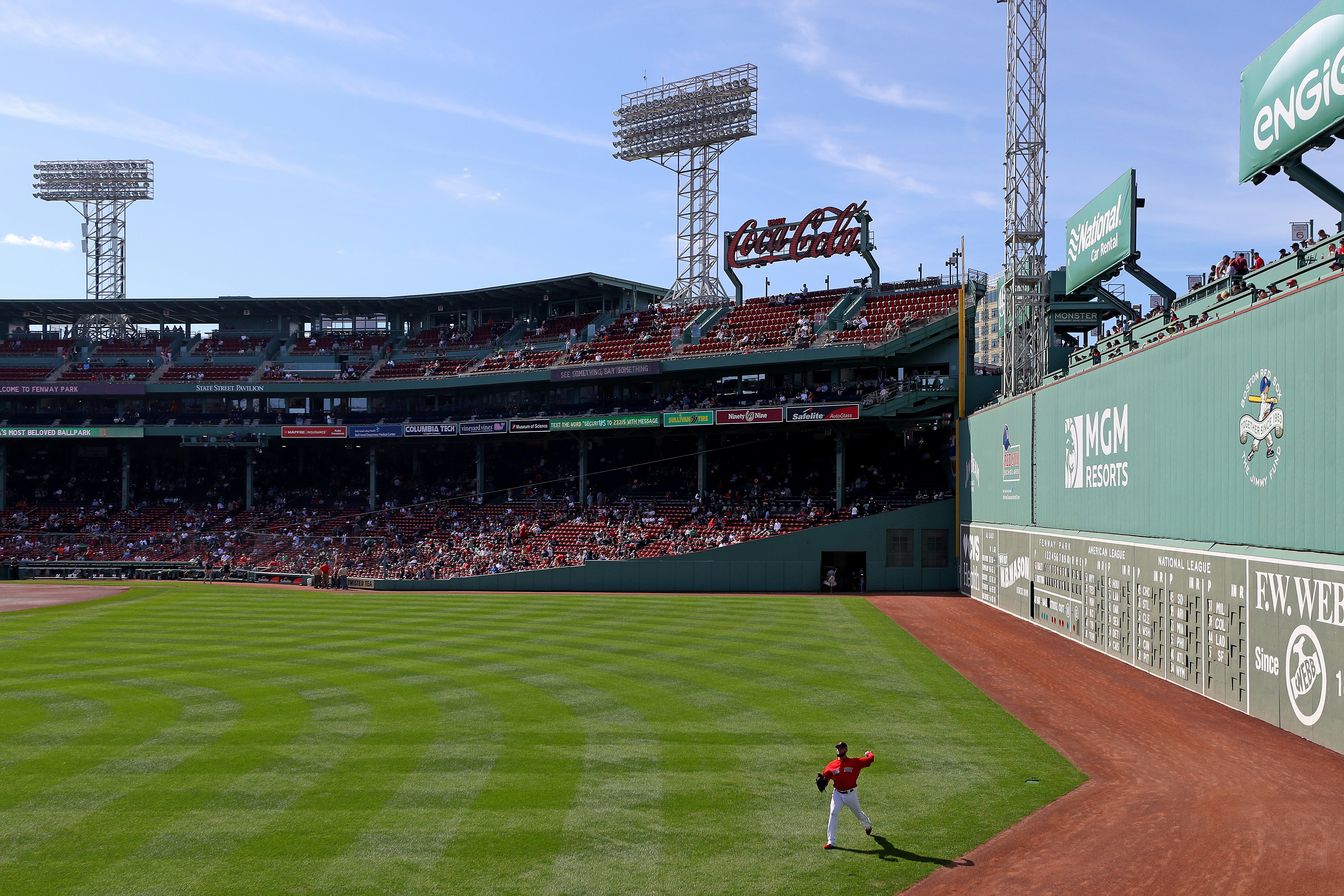 A baseball player fields a ball next to the large wall called the Green Monster in Fenway Park, Boston