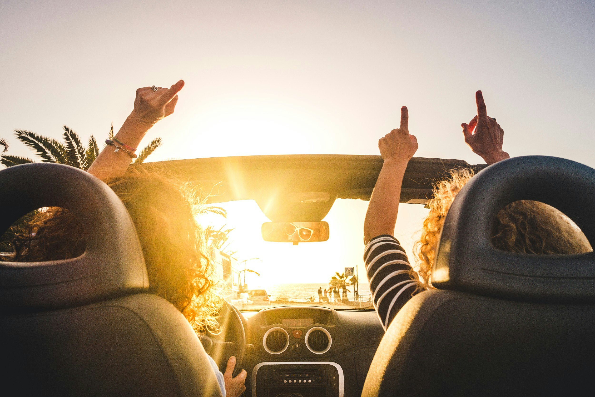 Two people riding in a convertible car with ther hands in the air