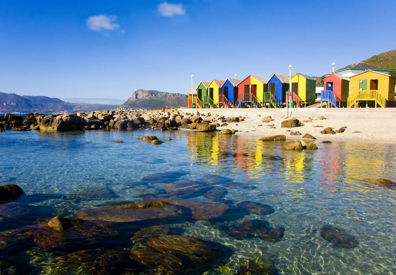 St James Beach with colourful bathing boxes on a sunny town, Cape Town. Table Mountain is visible in the background