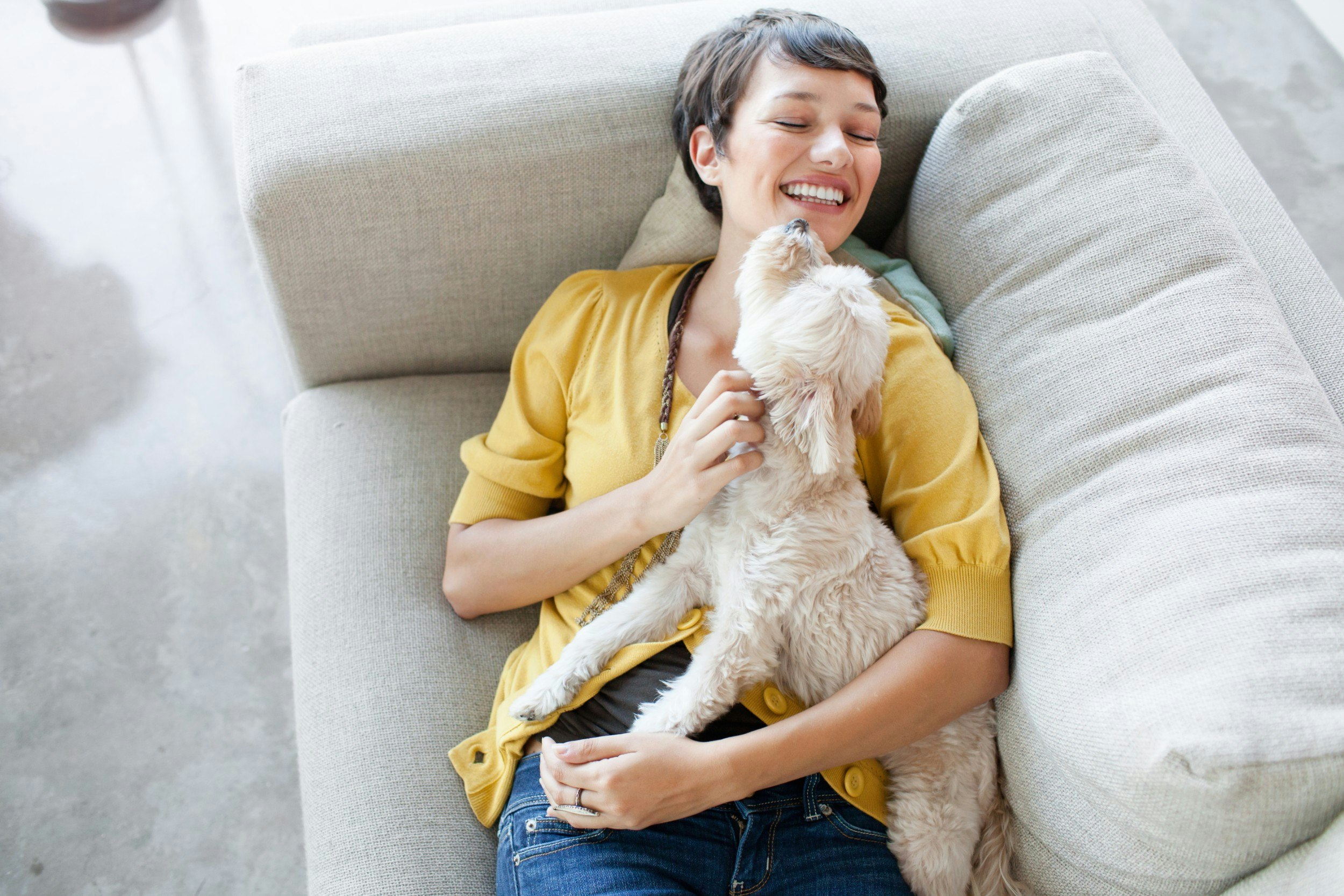 A woman lying on a sofa playing with her dog