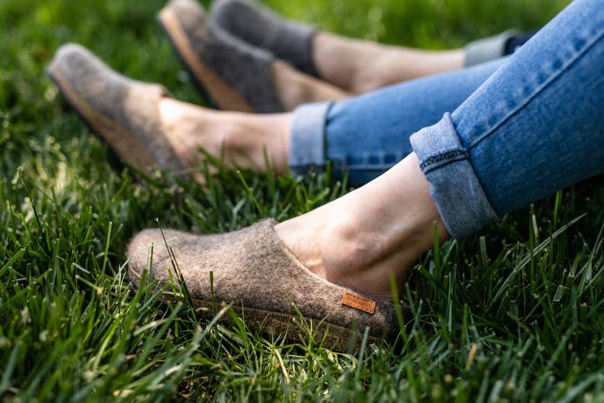 närbild av två personers underben, sittande i gräset, iklädda jeans och Stegmanns EcoWool träskor