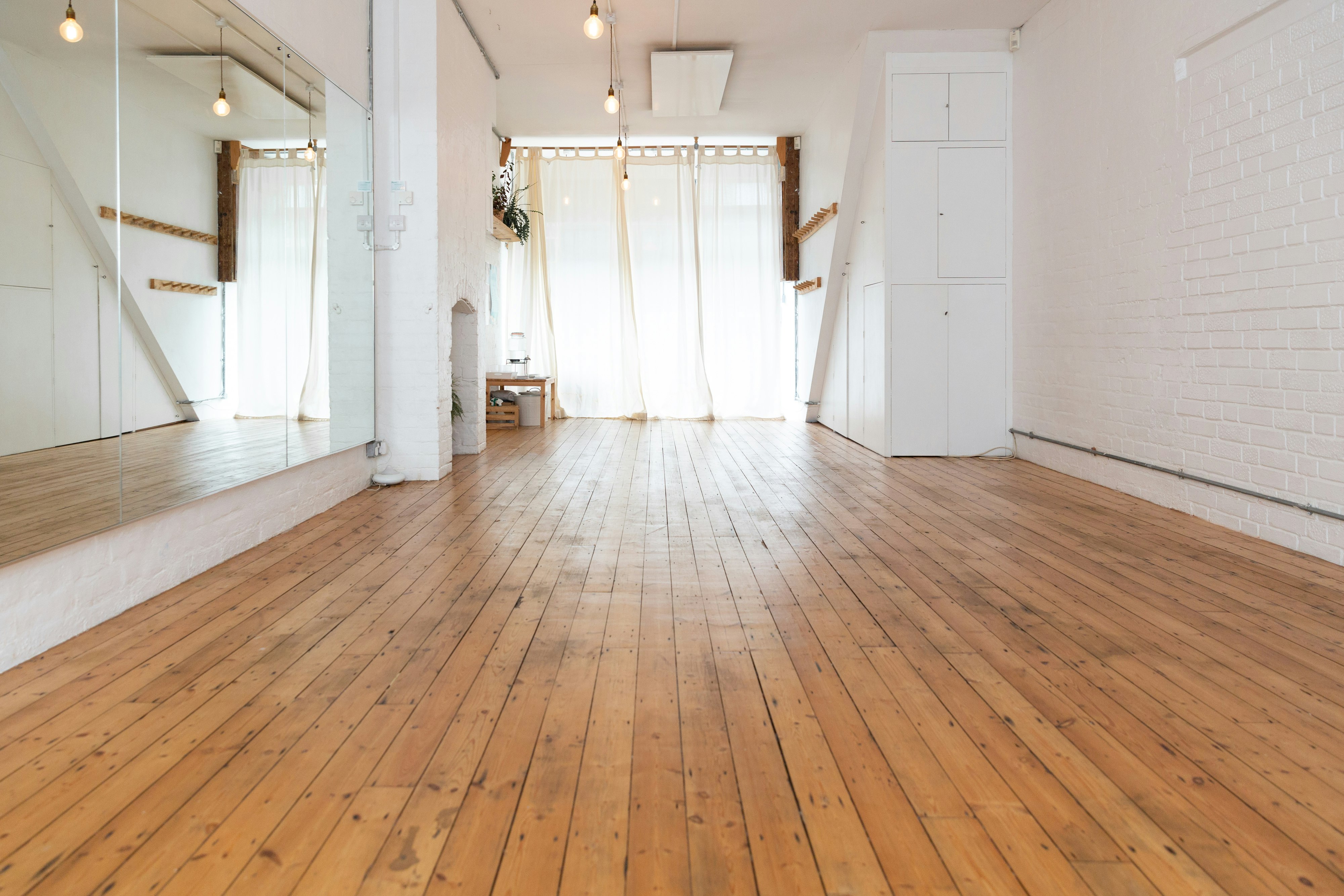 Stretch yoga studio with a hardwood floor, a mirrored wall on the left and a white wall on the right.