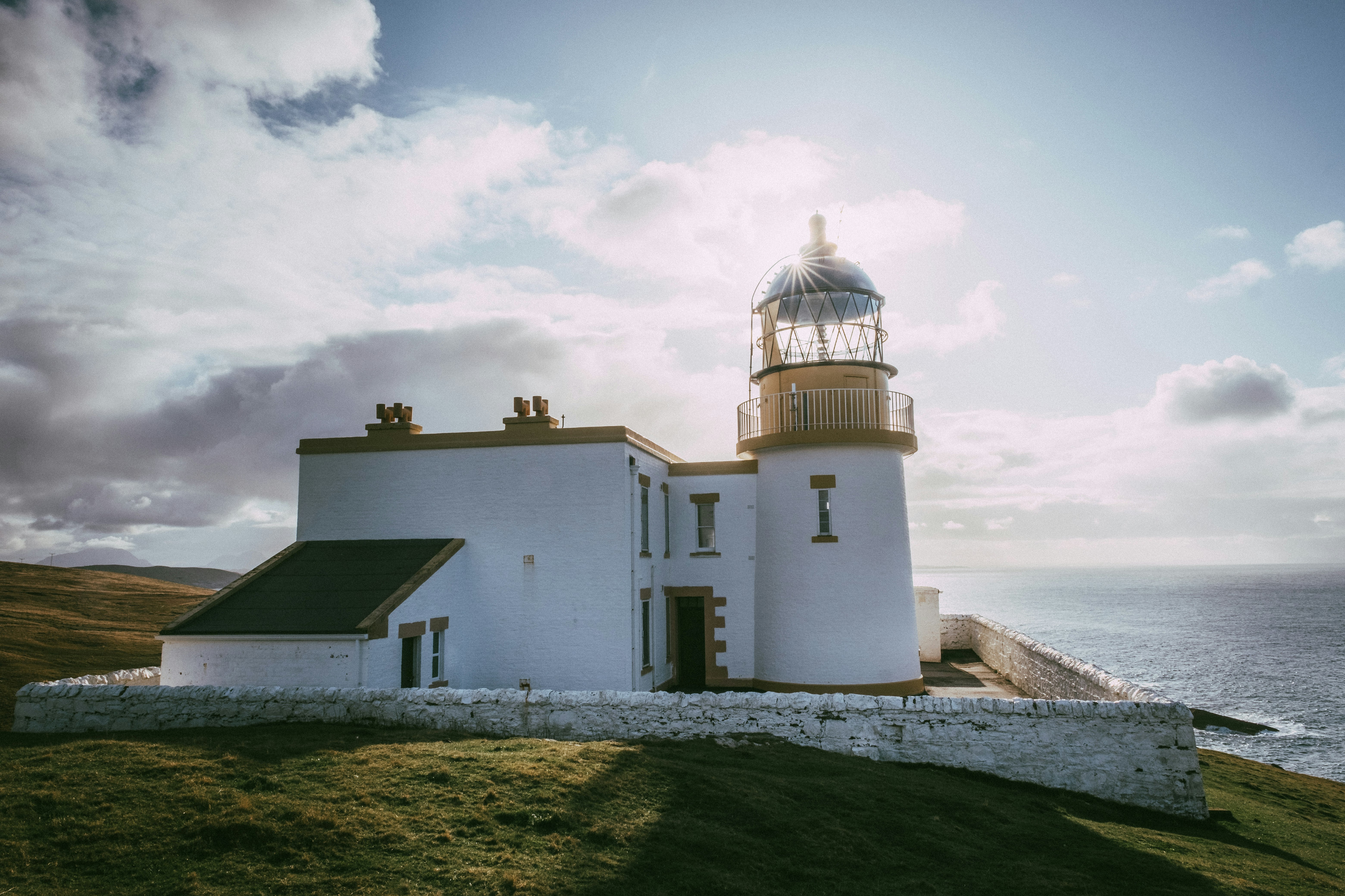 A photo of the side of Stoer Lighthouse during the daytime, underneath a cloudy sky.