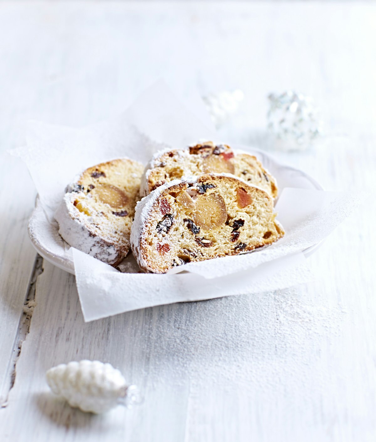 Three slices of Christmas stollen from Dresden served on a white dish and white wooden table.