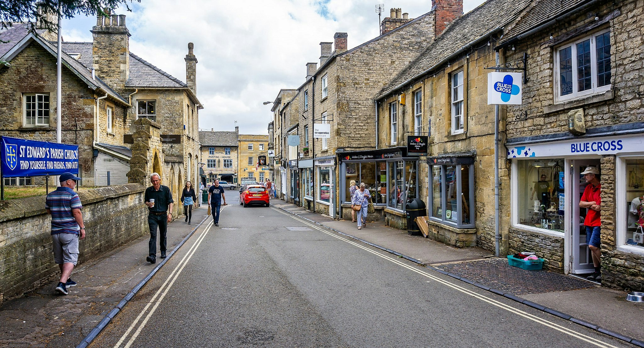 People walking down a high street past shops housed in quaint stone buildings.
