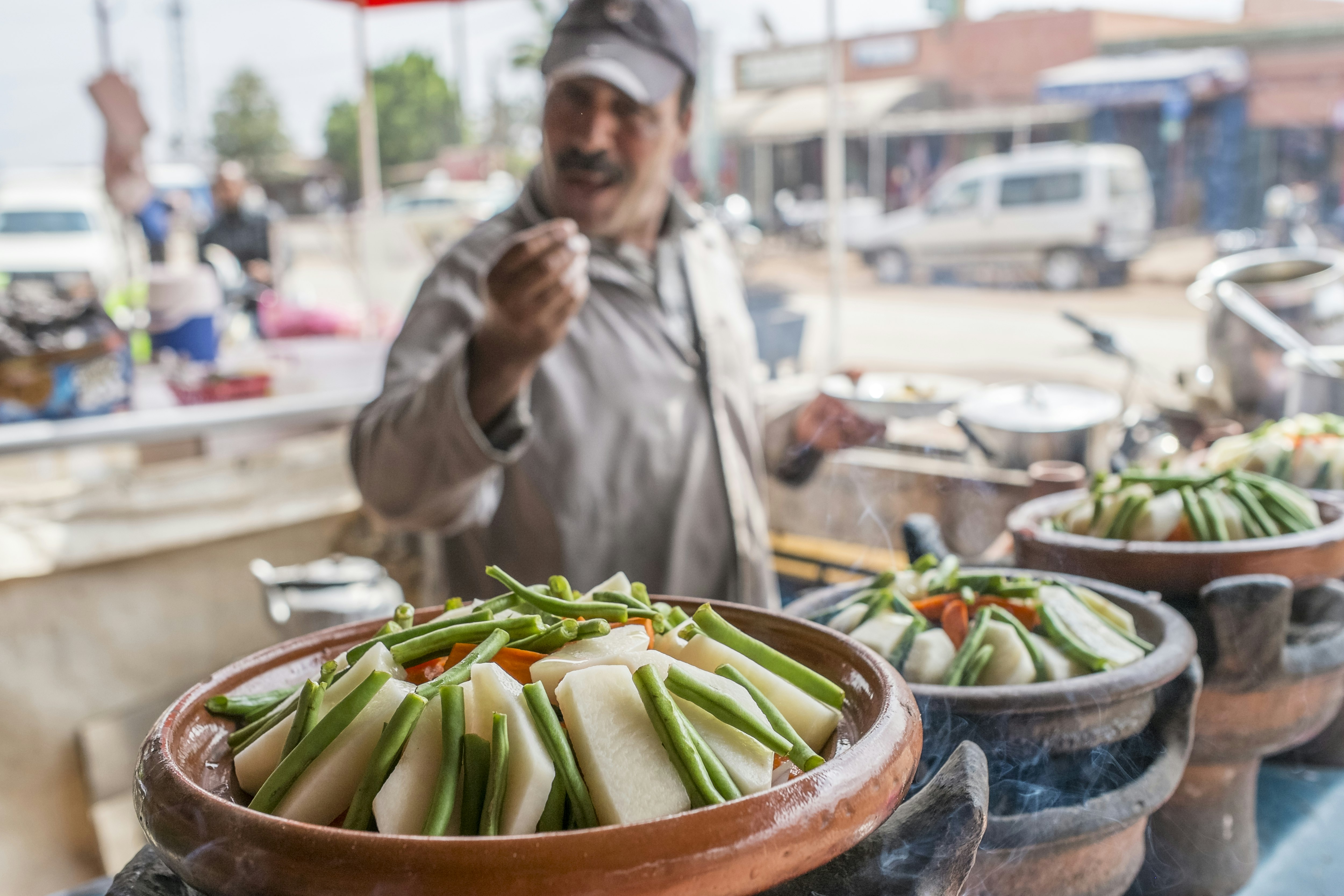 A man serving vegetables from clay pots at a traditional food stall in Marrakesh, Morocco