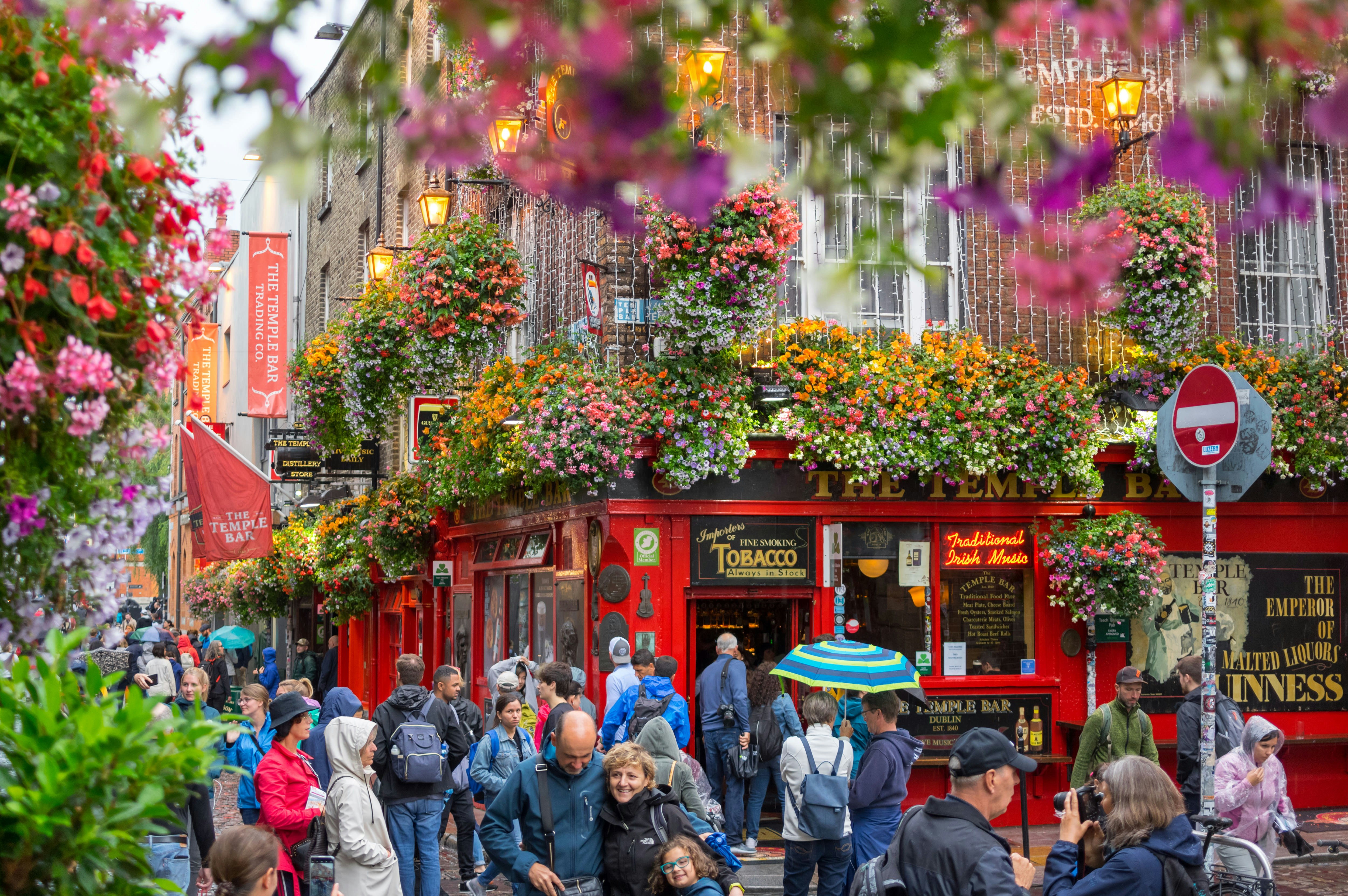 A colourful scene of crowds of people outside The Temple Bar in Dublin. Some walk along the streets while others gather to take photos.