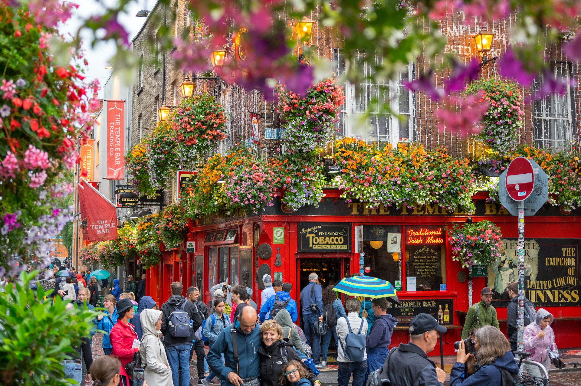 A colourful scene of crowds of people outside The Temple Bar in Dublin. Some walk along the streets while others gather to take photos.