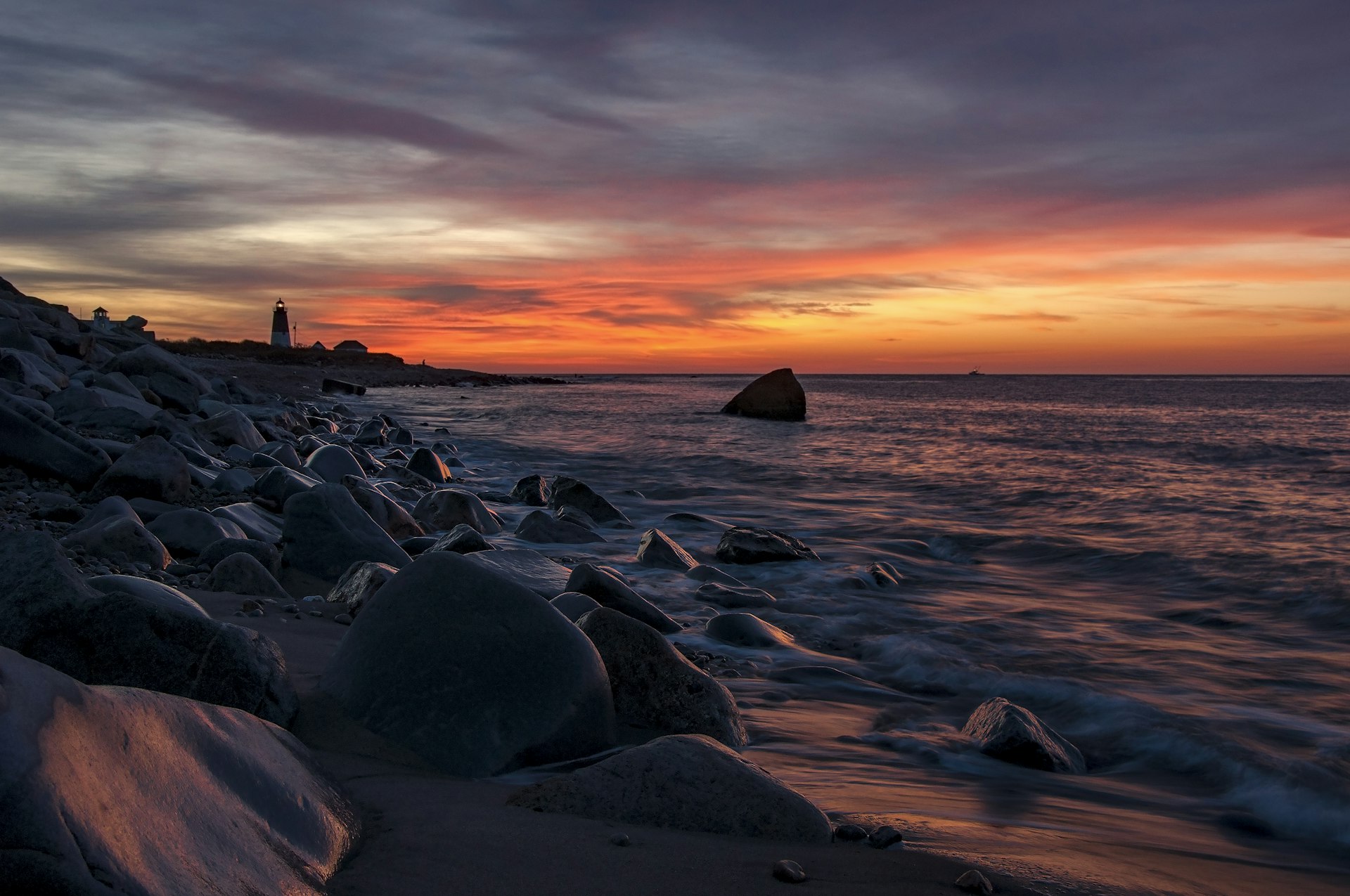 A pink and orange sunrise over a rocky shore with a lighthouse in the distance