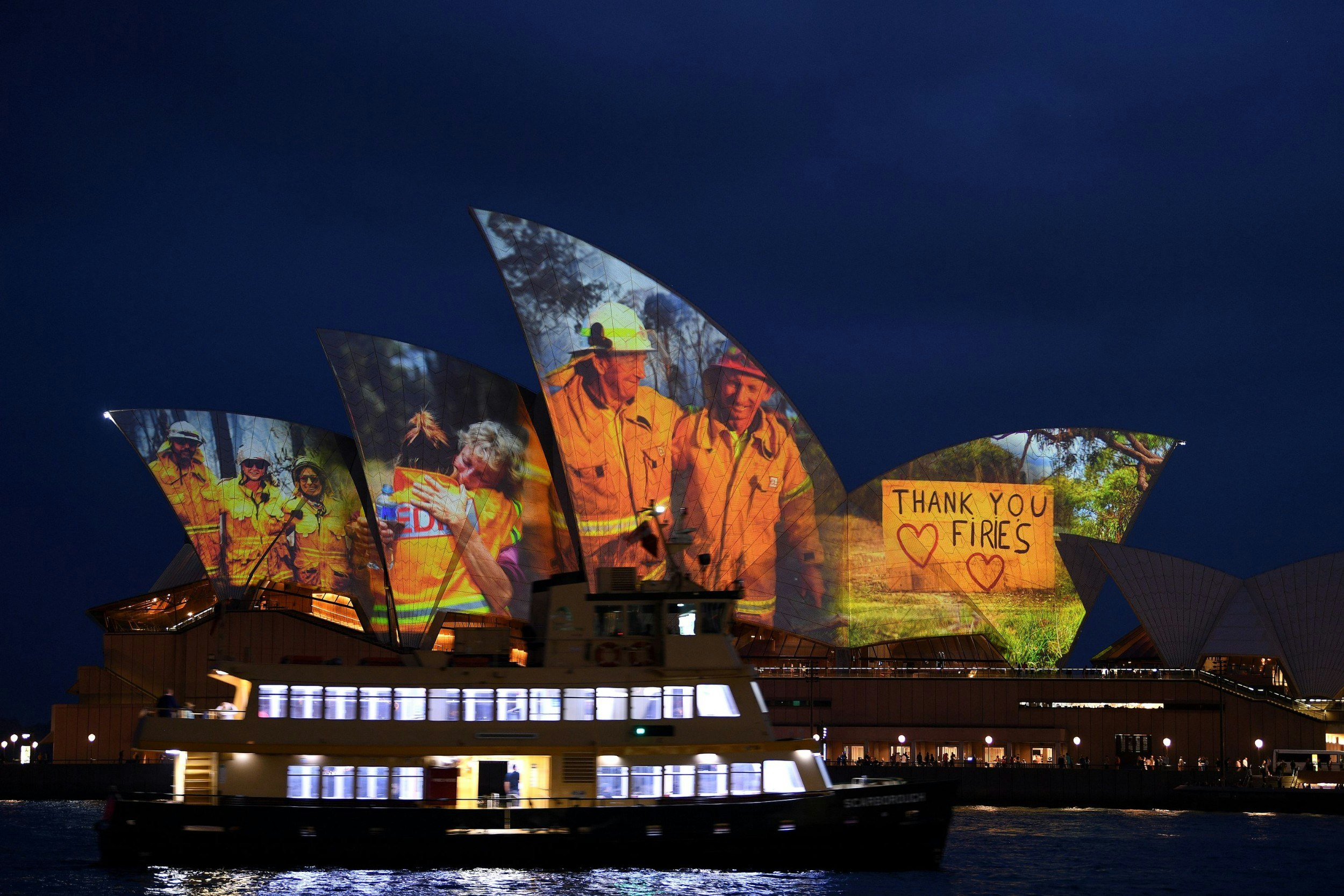 A cruise ship in front of the Sydney Opera House, which is lit up with a tribute to firefighters