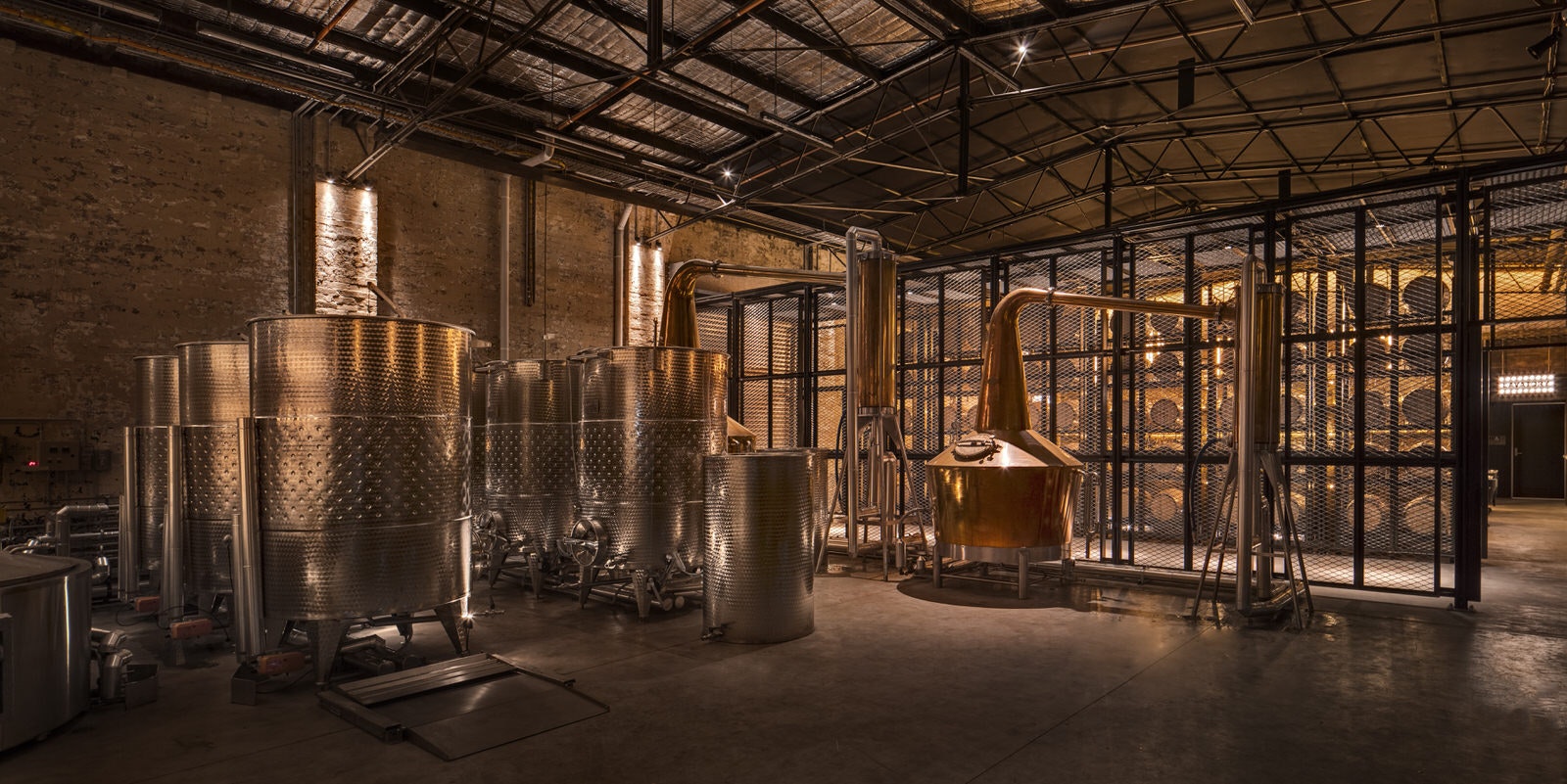 The warmly lit interior of Archie Rose distillery, Sydney, showing a small copper still and large steel washbacks. 