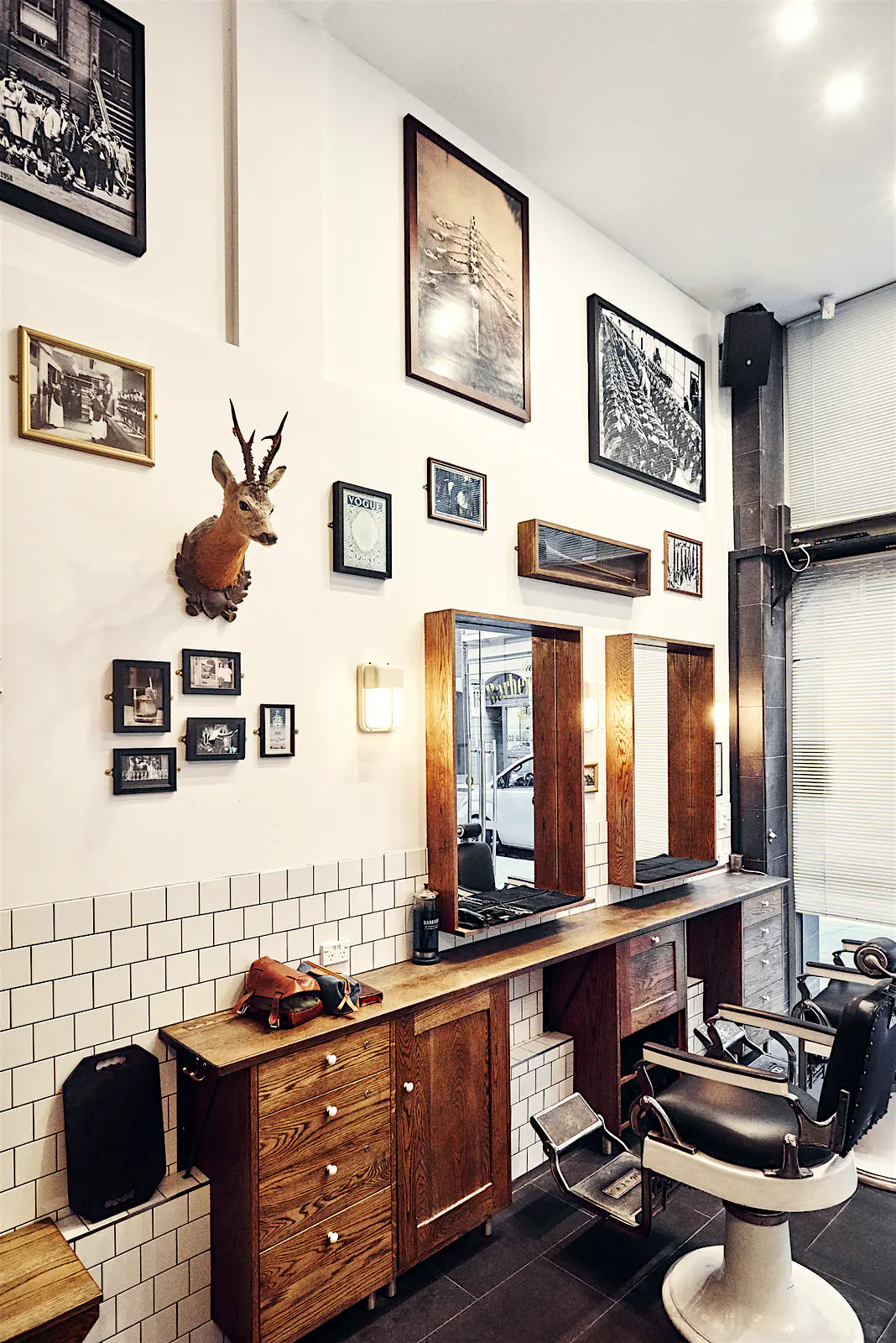 Sydney-gin_Barber-Shop.jpg An old-fashioned barber shop interior with white tiled walls, framed photos, a small mounted deer's head and barbershop chairs