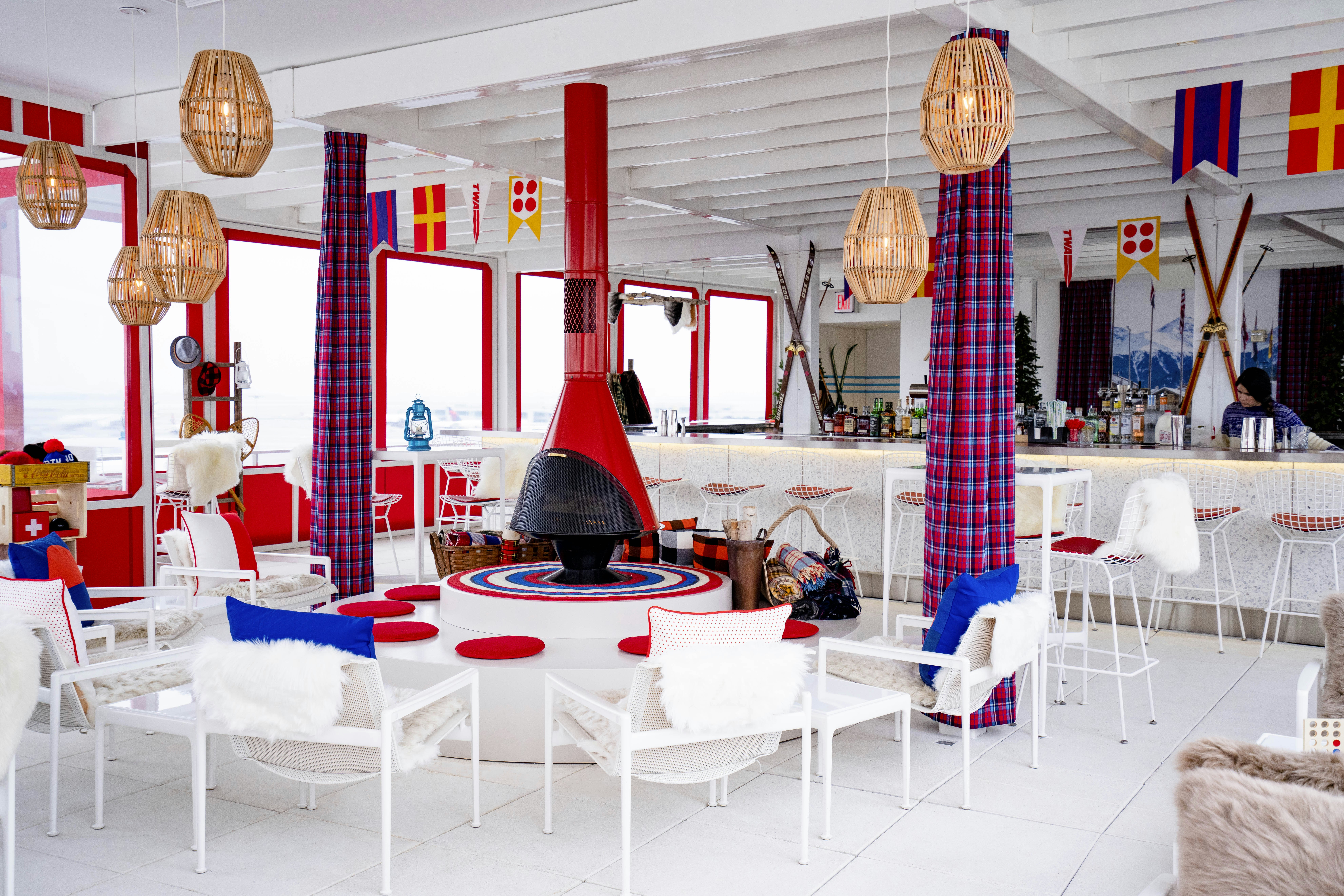 TWA Hotel Runway Chalet at The Pool Bar interior bar with white chairs, the red fireplace, and rattan light fixtures