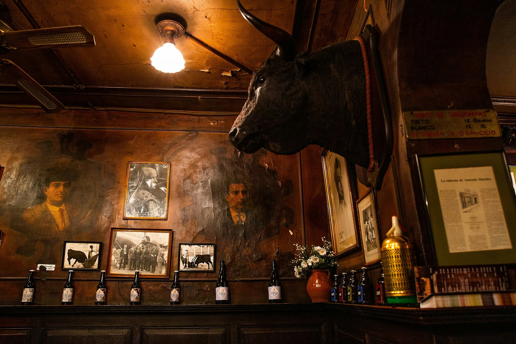 Ett enormt tjurhuvud hänger på den mörka träväggen i Taberna Antonio Sánchez, Madrid;  en annan vägg är kantad med gamla fotografier och flaskor.