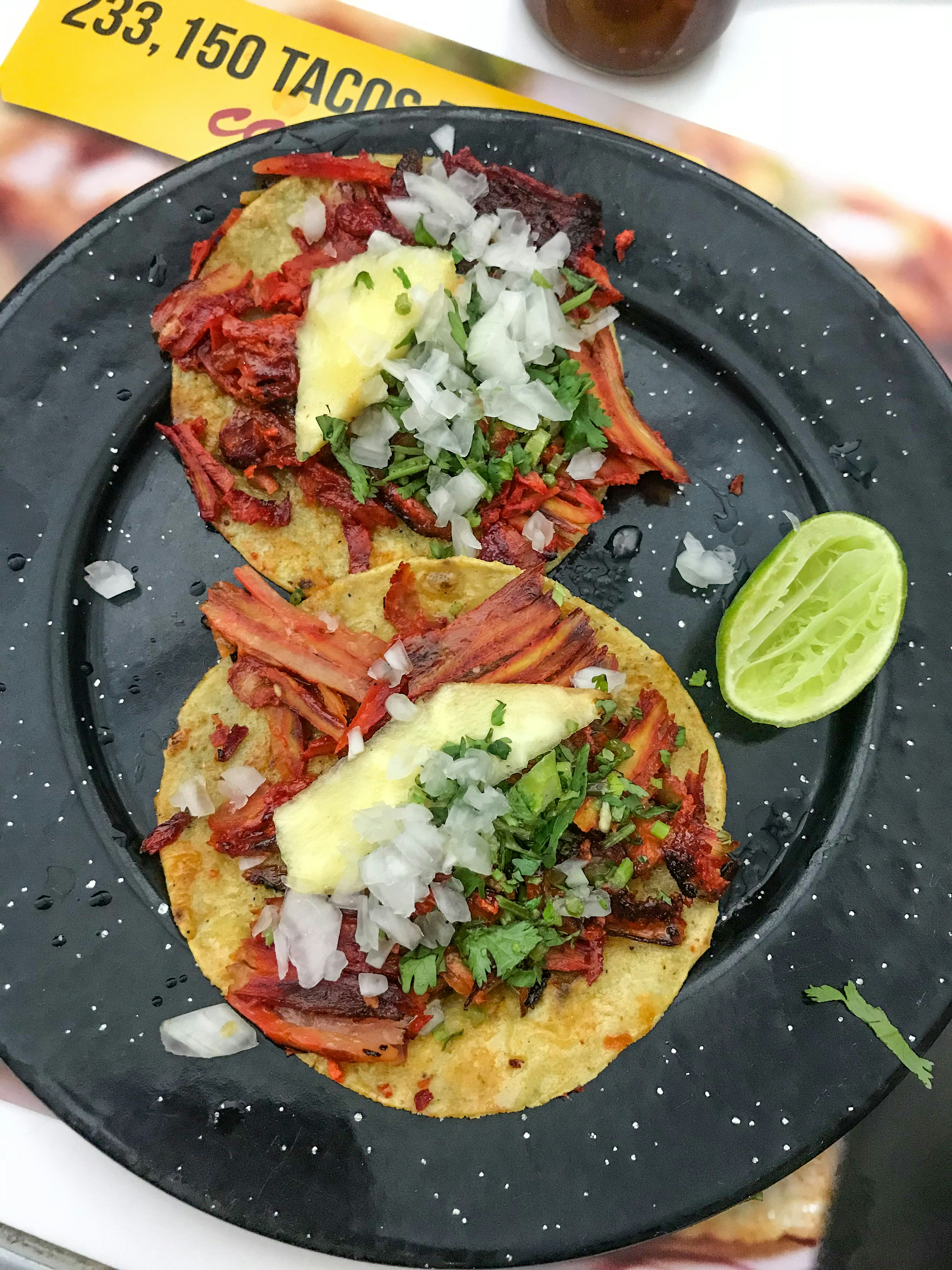 Two tacos with grilled meat, pineapple and cilantro on a red plate