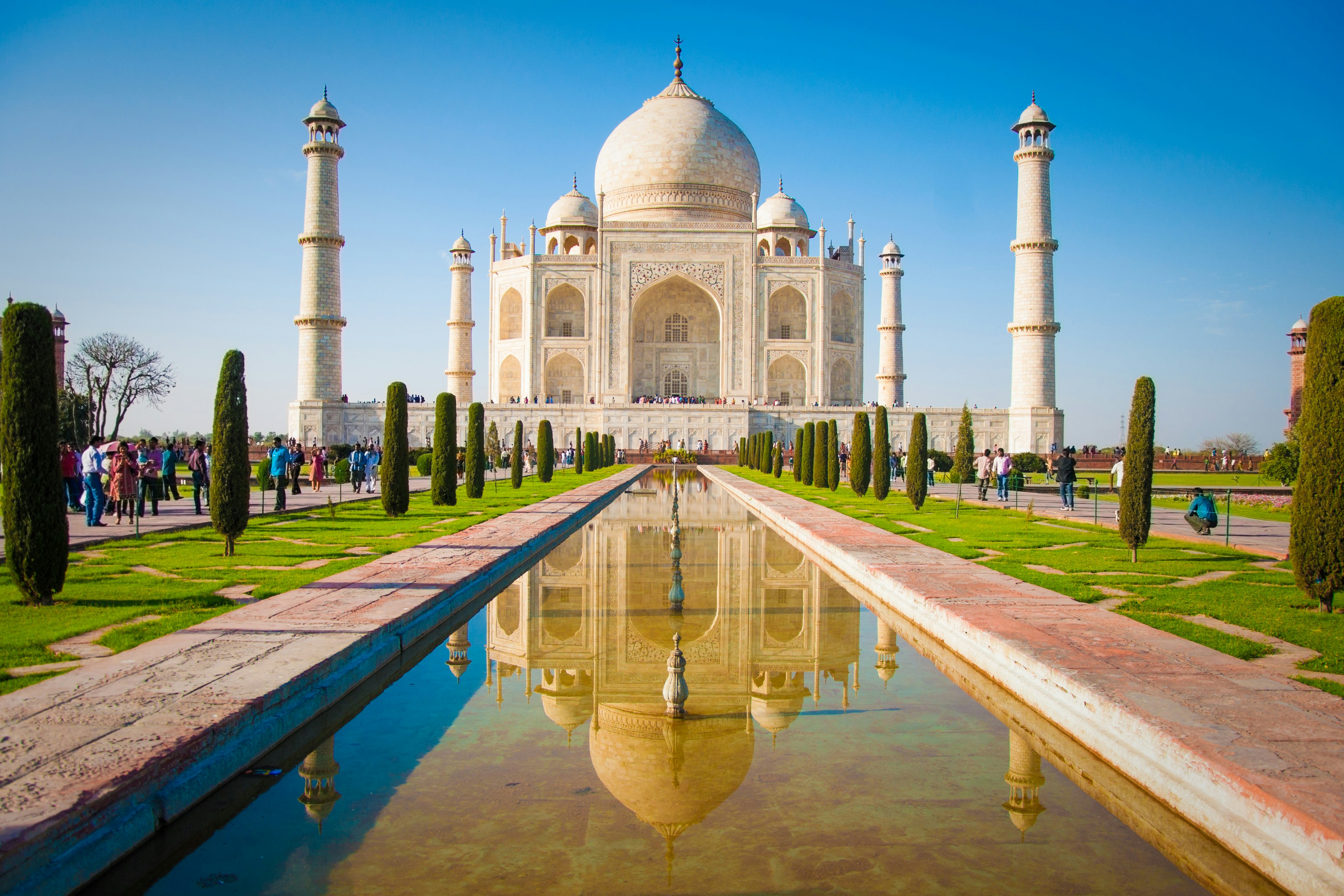 A channel of water leads through ornamental gardens to the Taj Mahal, a huge domed white marble monument with white minarets at each corner.