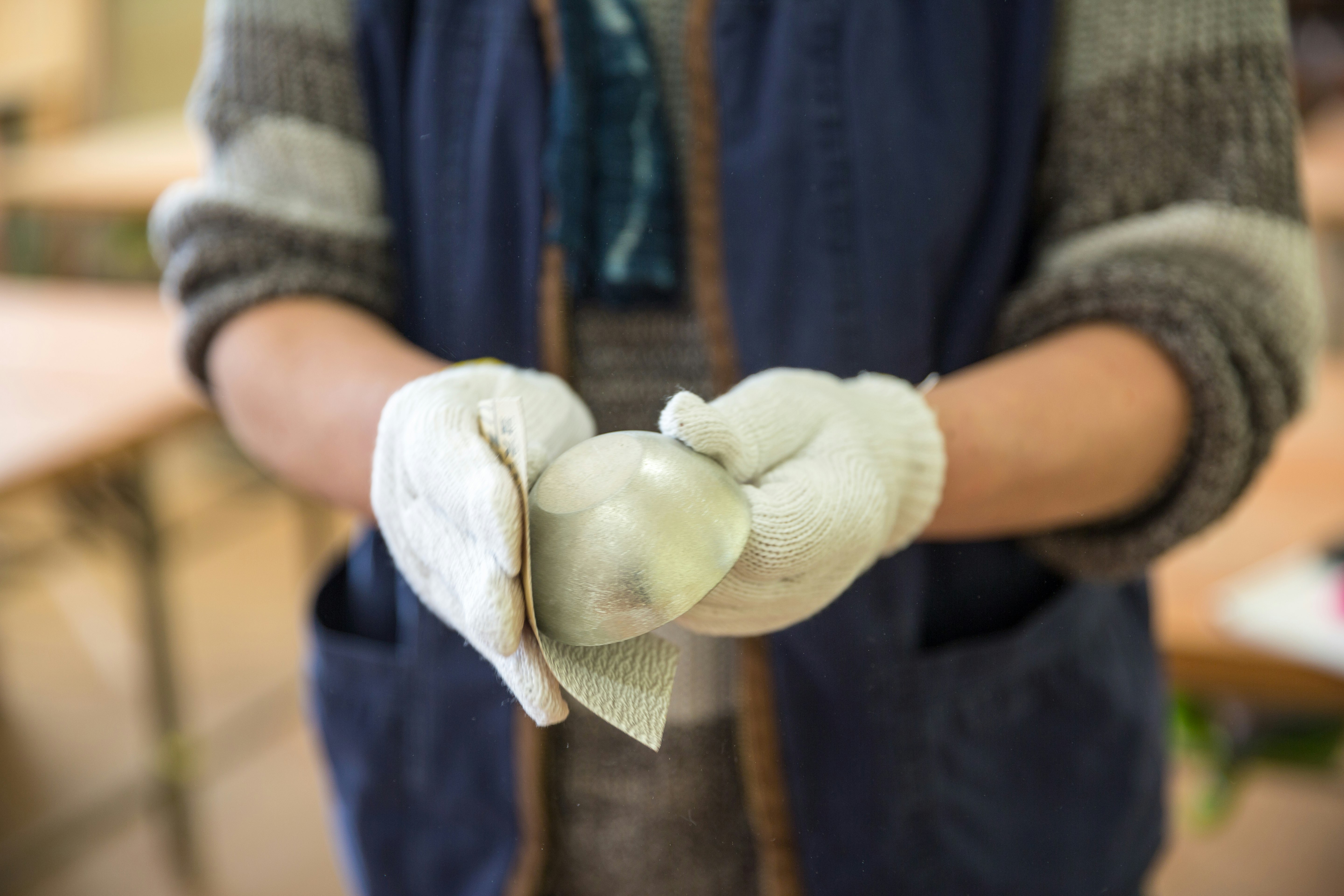 A close-up image of gloved hands sanding down a copper sake cup