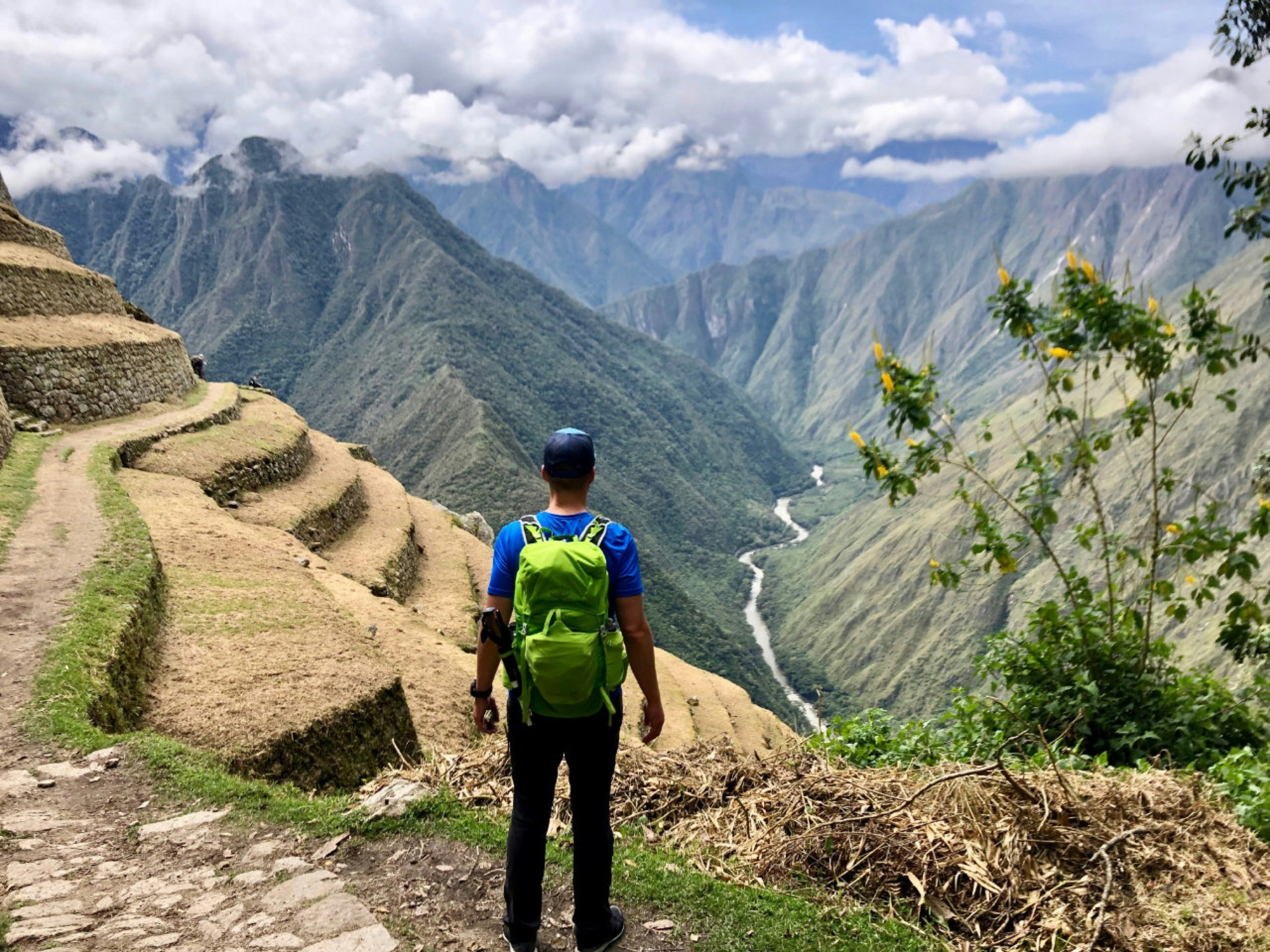 A man stands on a bluff looking over terraced mountains on the Inca Trail of Peru, with a river far below; Upping your travel game