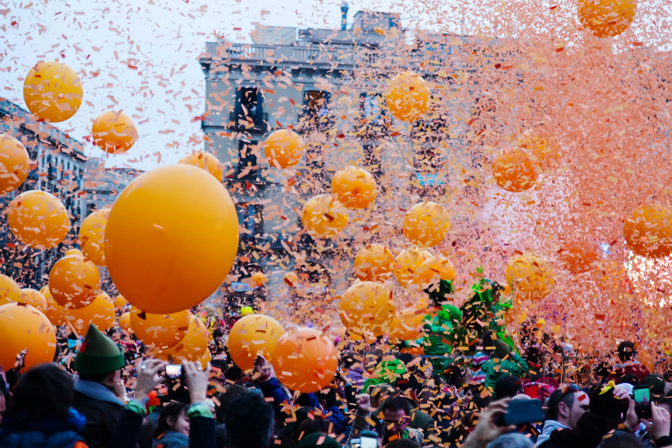 A crowd stands under a shower of orange confetti in Barcelona, as large orange balloons float in the air.