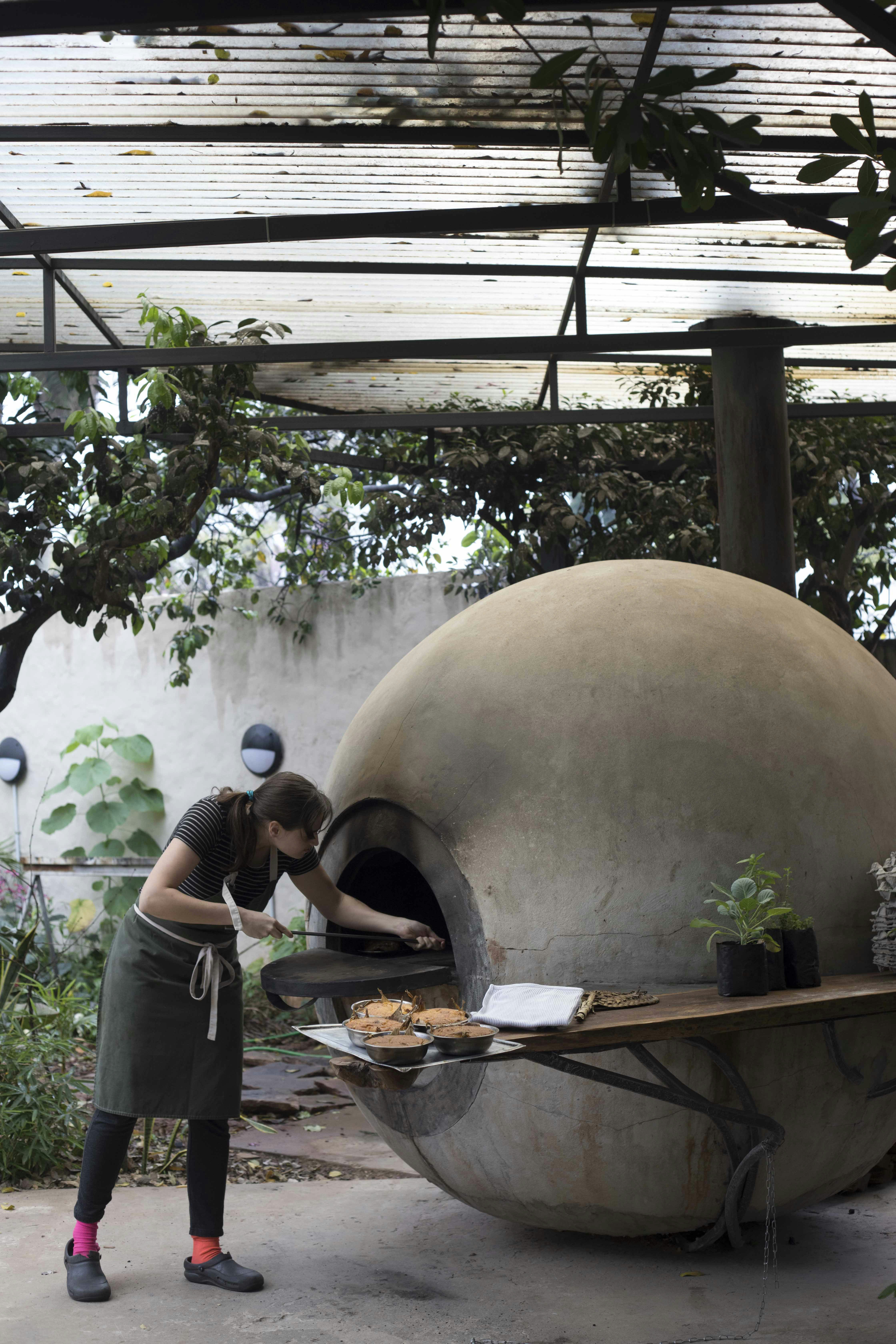 A woman pushes a tray into a large white stone oven in the shape of a sphere called a tatakua outside the Pakuri restaurant in Paraguay 