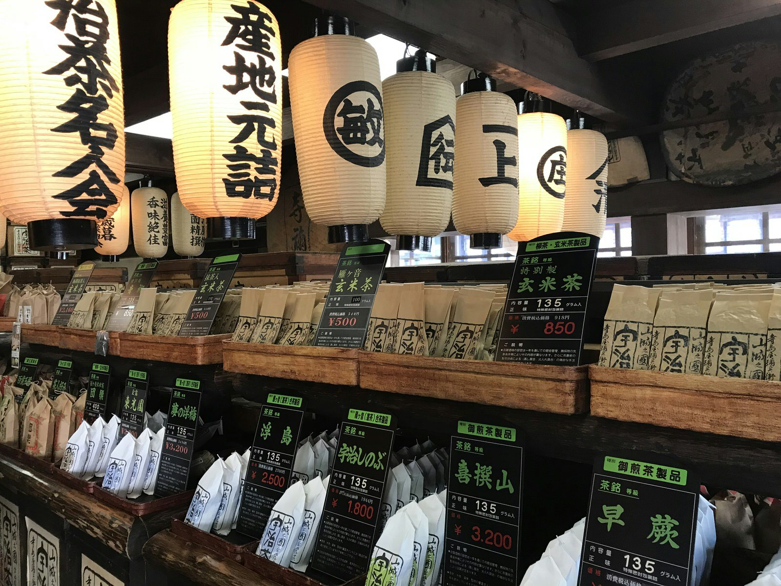 Bags of tea are arranged on wooden shelves with signs explaining each type of tea in Uji, Japan. 