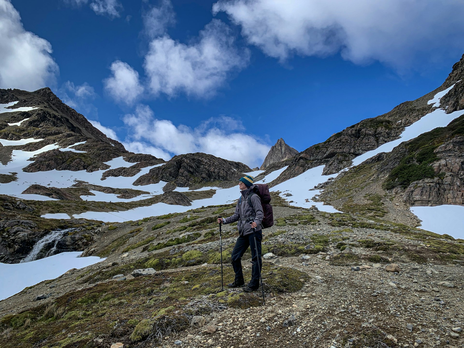 A hiker stands on a trail with mountains and blue skies in the distance.