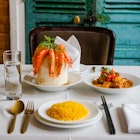 A table is set with dishes, cutlery and a glass of water. One dish is filled with yellow rice, another filled with vegetables and meat in an orange sauce and third has cooked shrimp dangling from a circular dish.