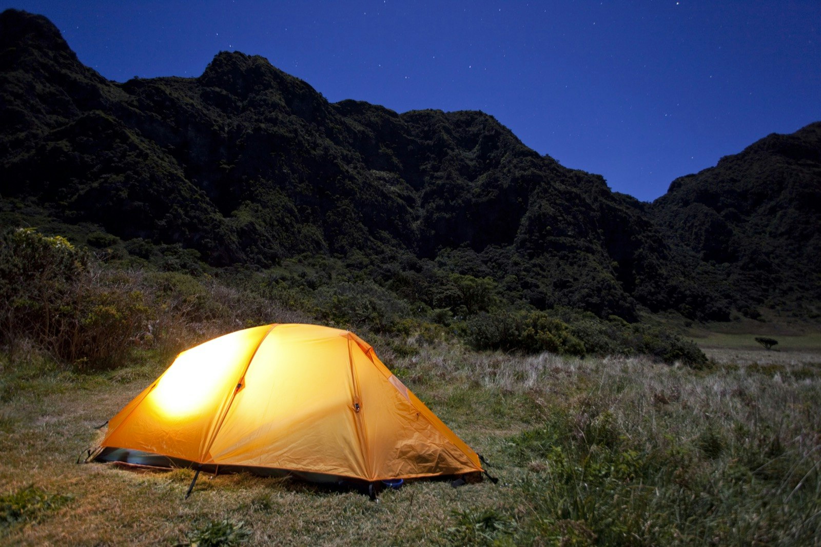 A glowing orange tent in Haleakala National Park surrounded by black peaks and a deep blue night sky.jpg