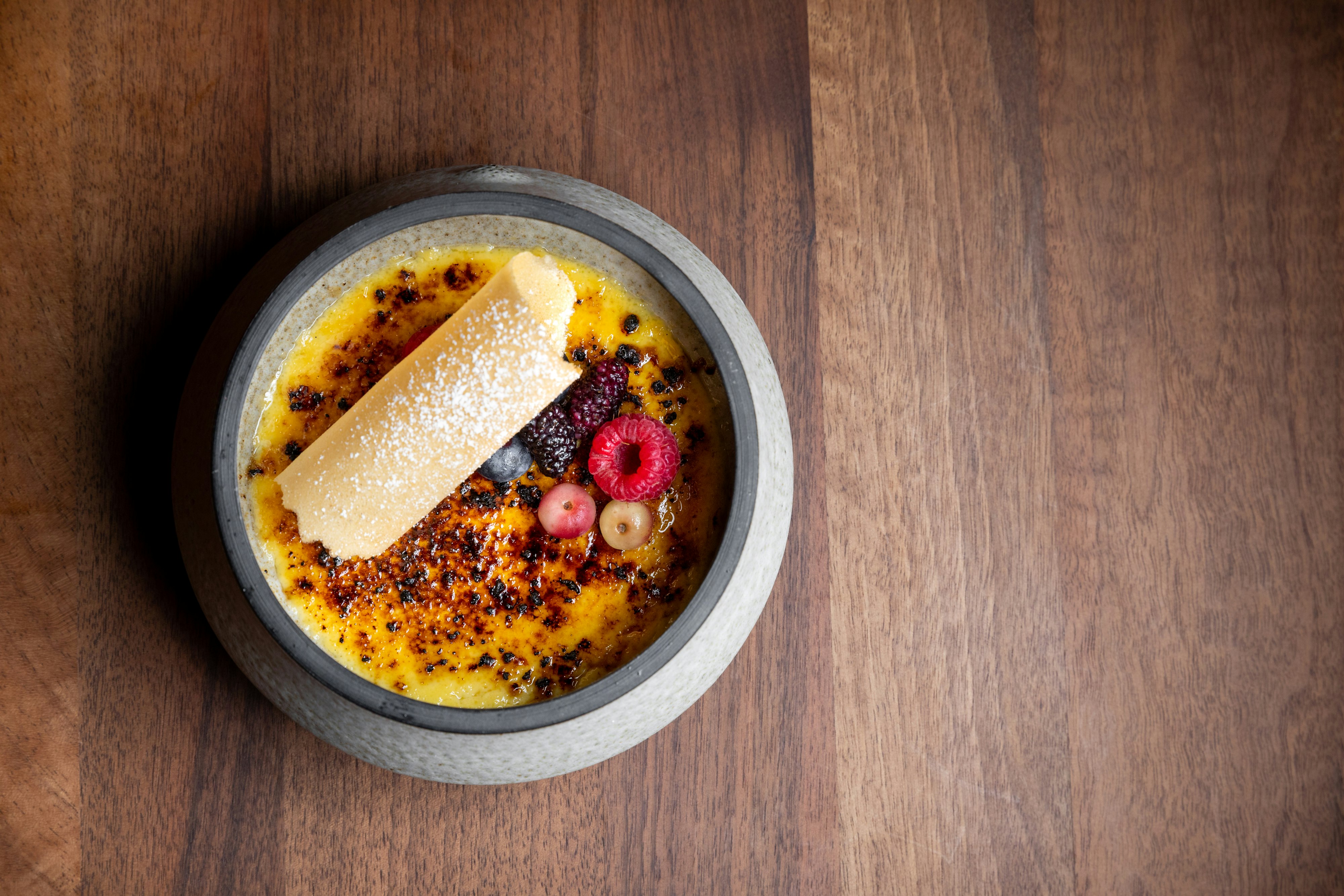 A duck egg creme brulee dish with berry topping and flecks of powdered sugar