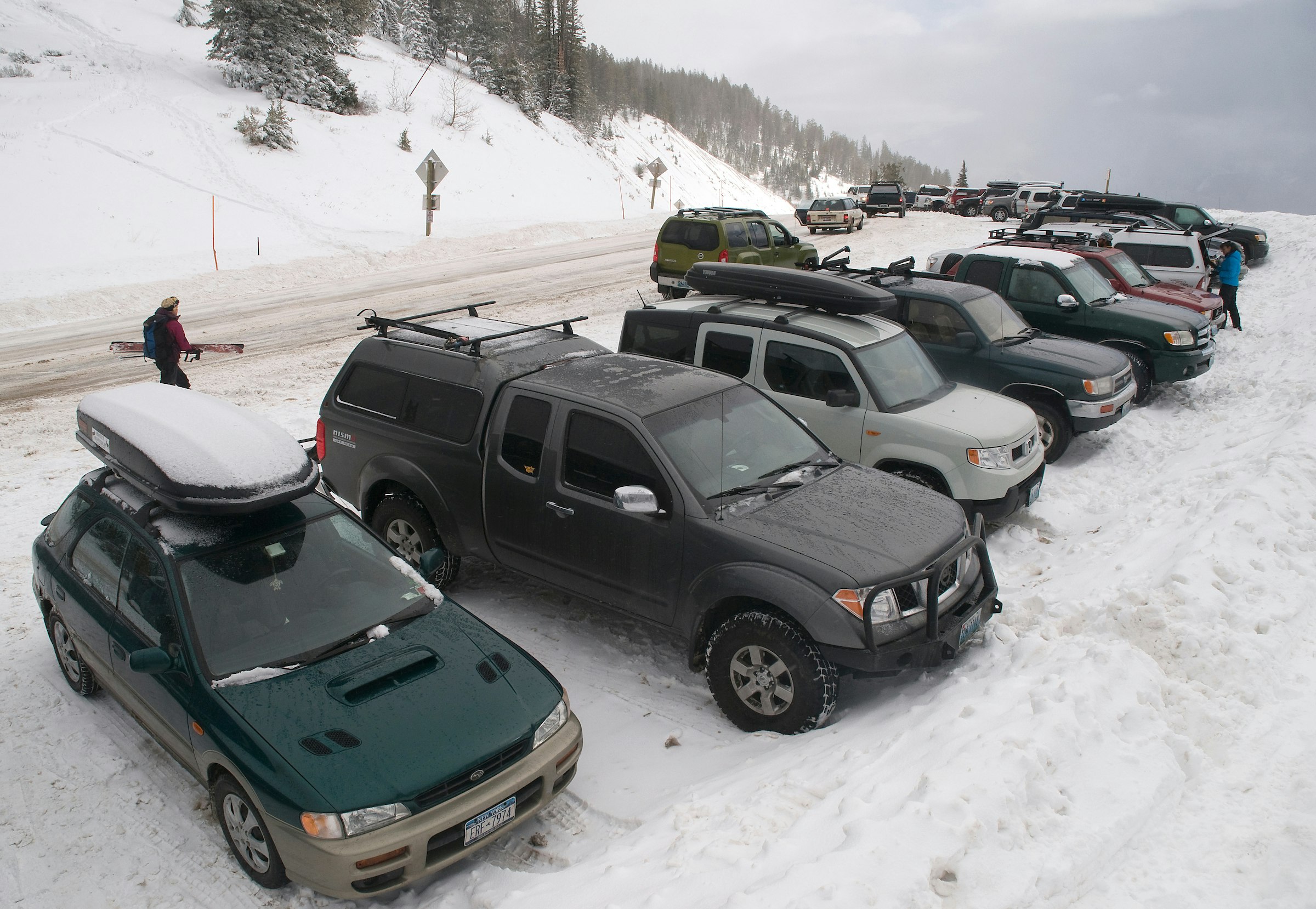 A row of parked cars stretches as far as the eye can see on a snow-covered road