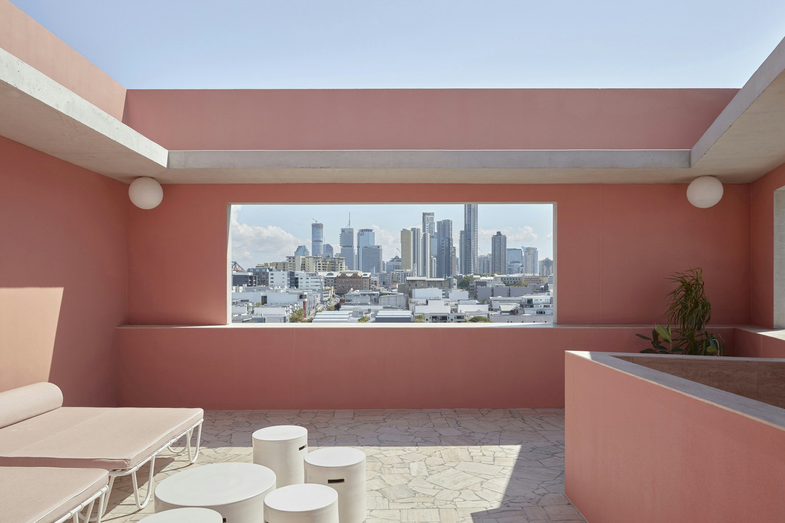 Brisbane's skyline pictured through a large rectangle gap in a pink wall on The Calile's rooftop