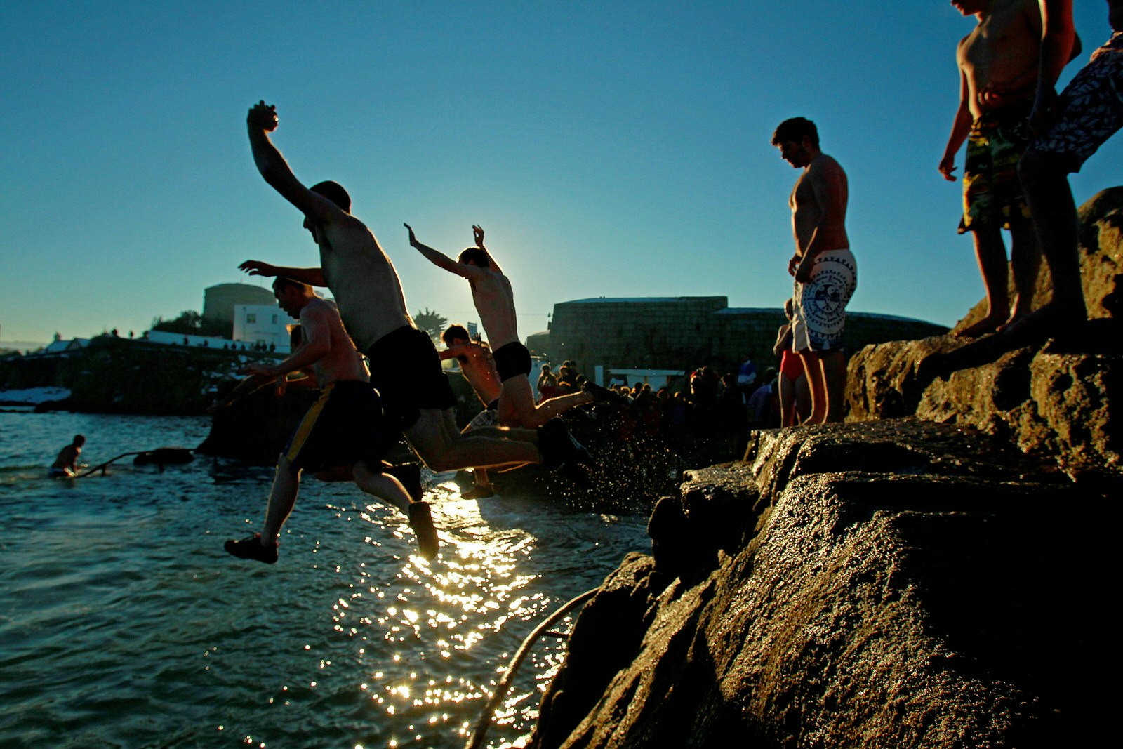 A group of people wearing bathing suits are jumping off the forty foot on a sunny day. 