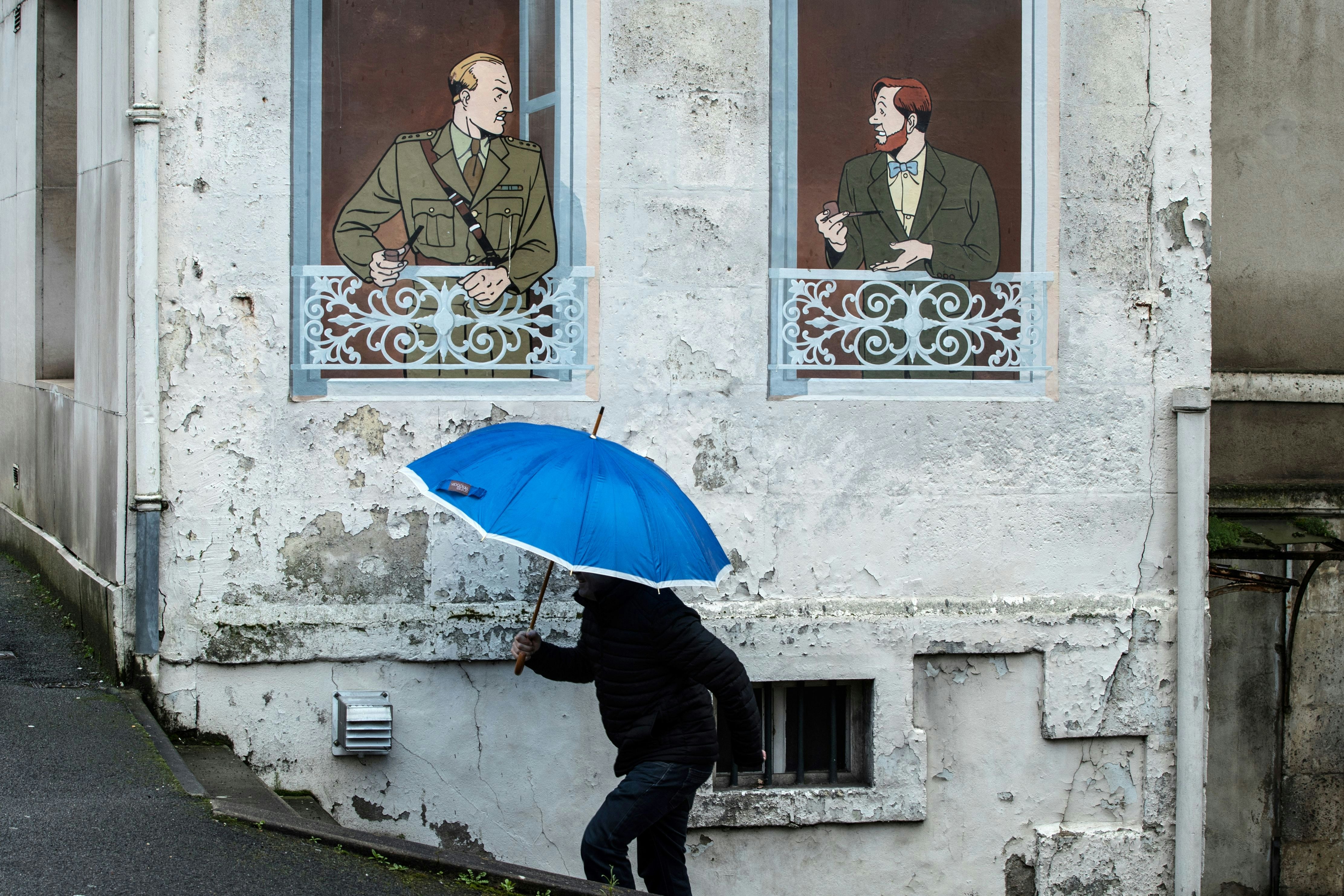  A man walks past a wall with comic book characters Blake and Mortimer 