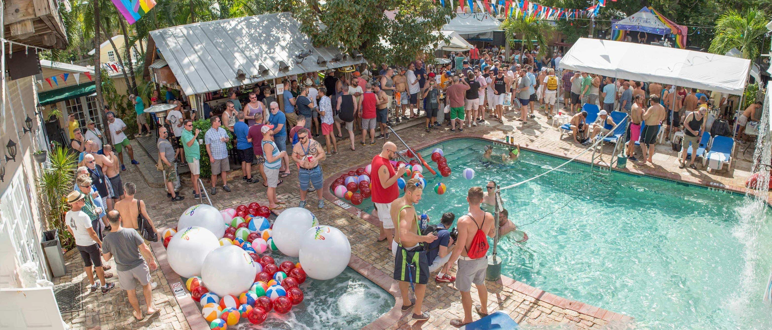 Clothed revelers surround the pool and hot tub at the Garden Bar at the Bourbon Street Pub, where a small covered outdoor bar and sun pavilions are strewn with red and blue streamers and gay pride flags. In the hot tub and pool are dozens of beach balls in every color and size.