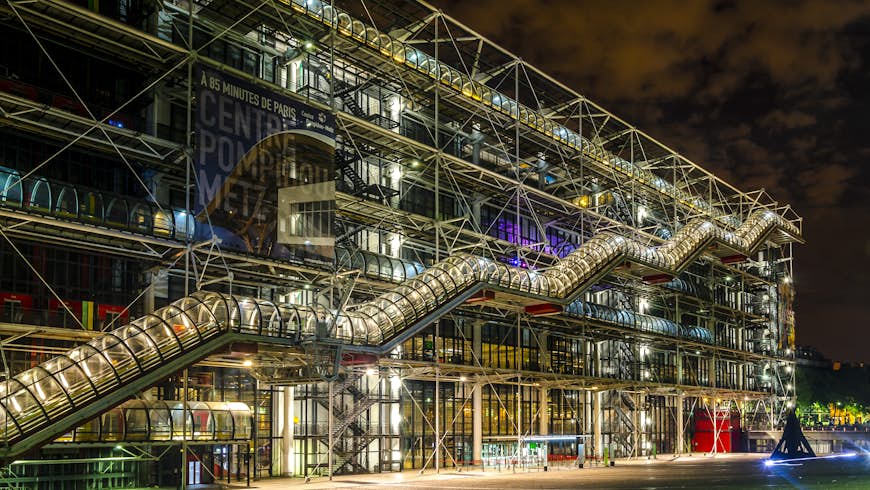 A night view of the Pompidou Centre. A stair that resembles a tube is visible going up the side of the building. 