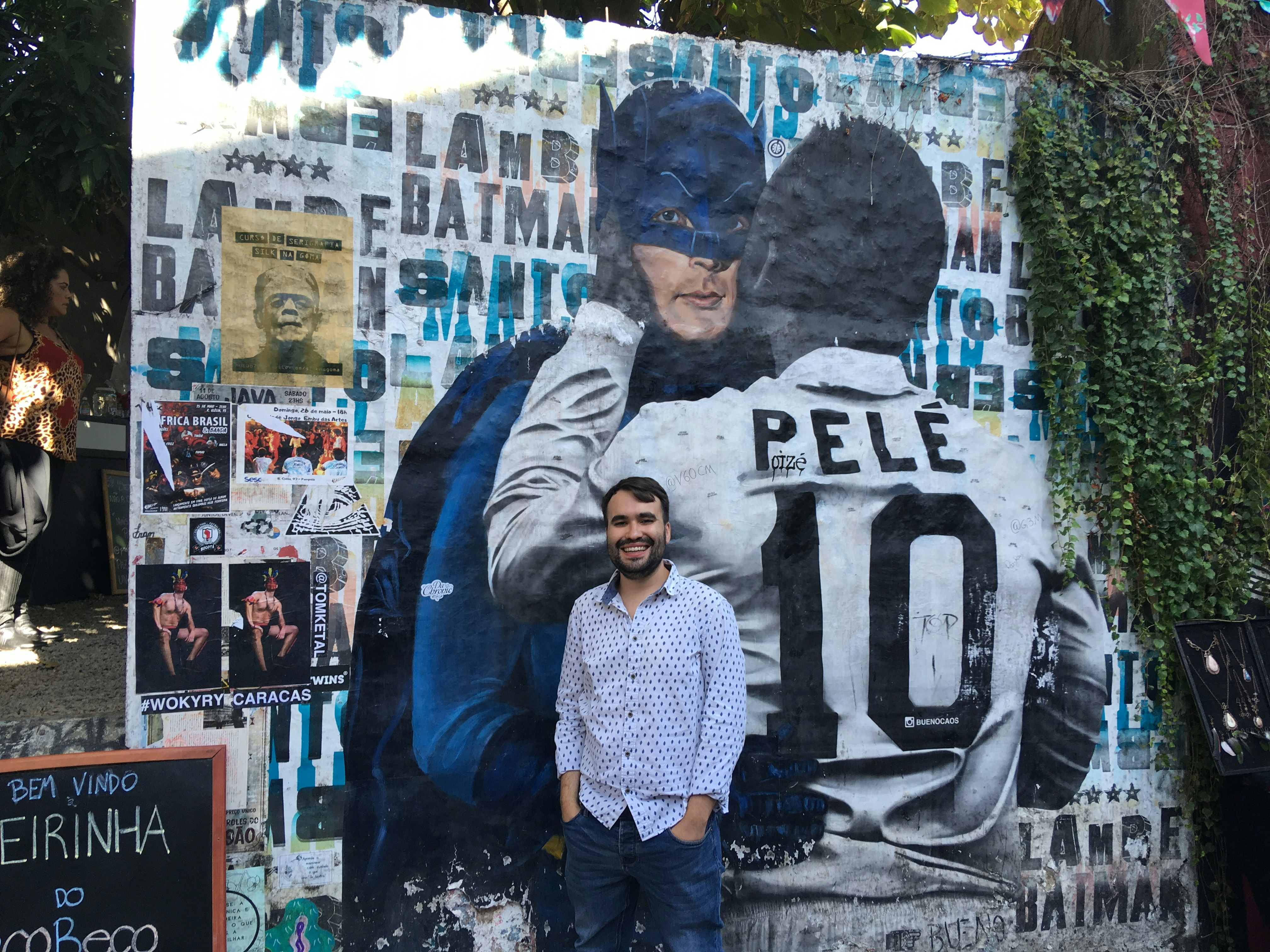 Joe Revill stands in front of a mural of Batman and Pele at Beco do Batman. 