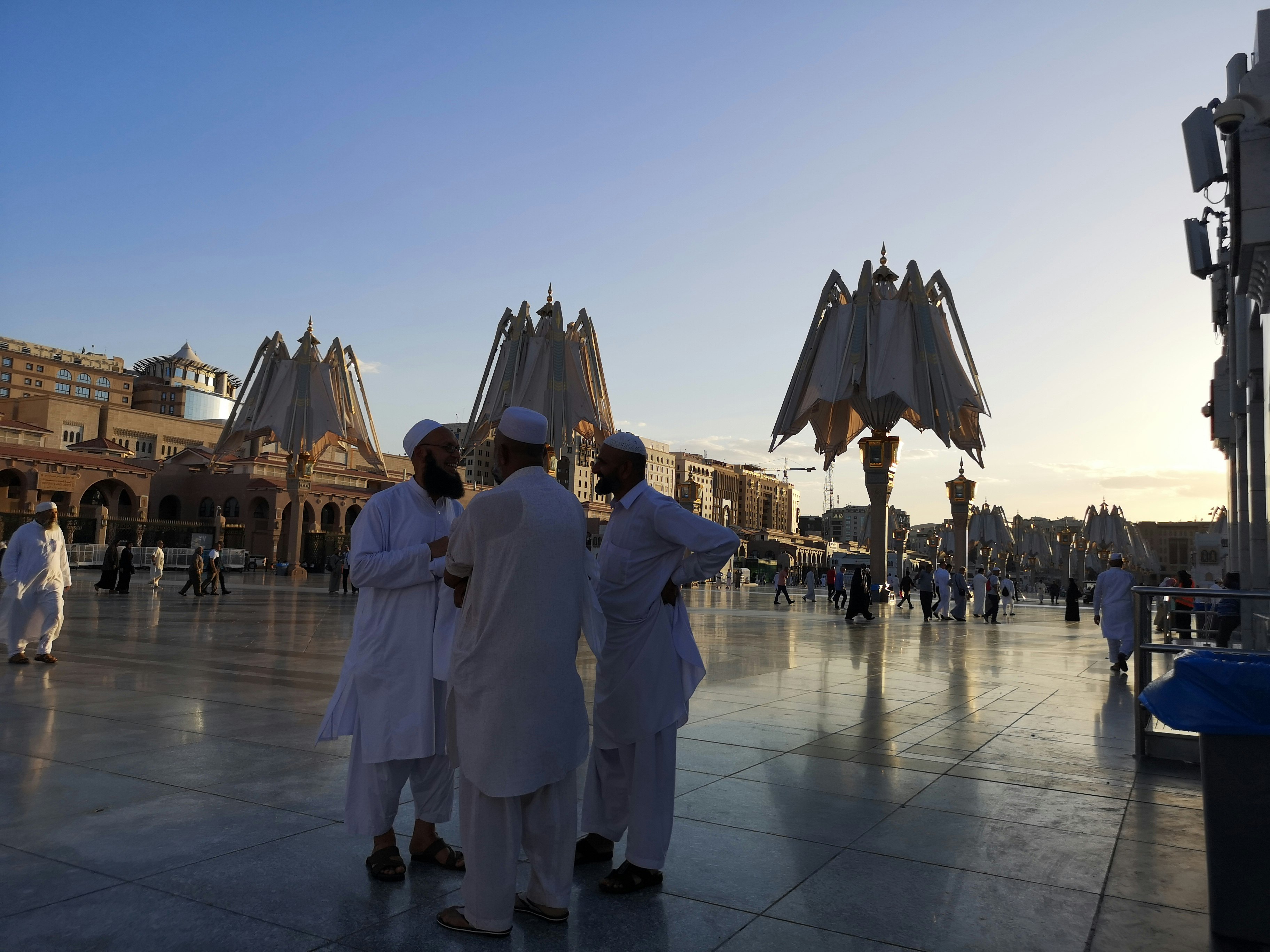 A group of men stand around the mechanical parasols at the mosque closing at sunset