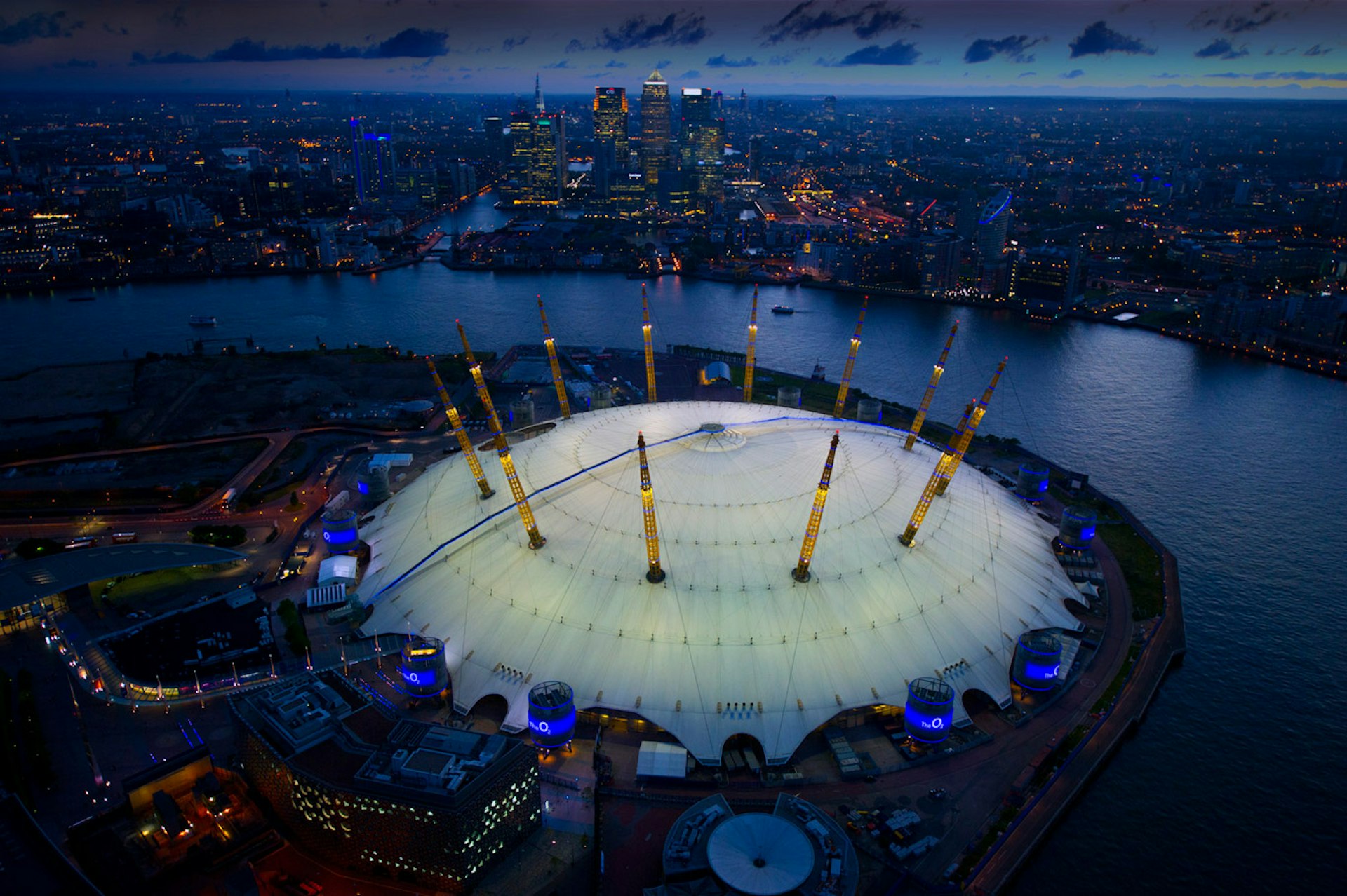 An aerial night-time view over the O2, a huge domed arena next to the River Thames in London.