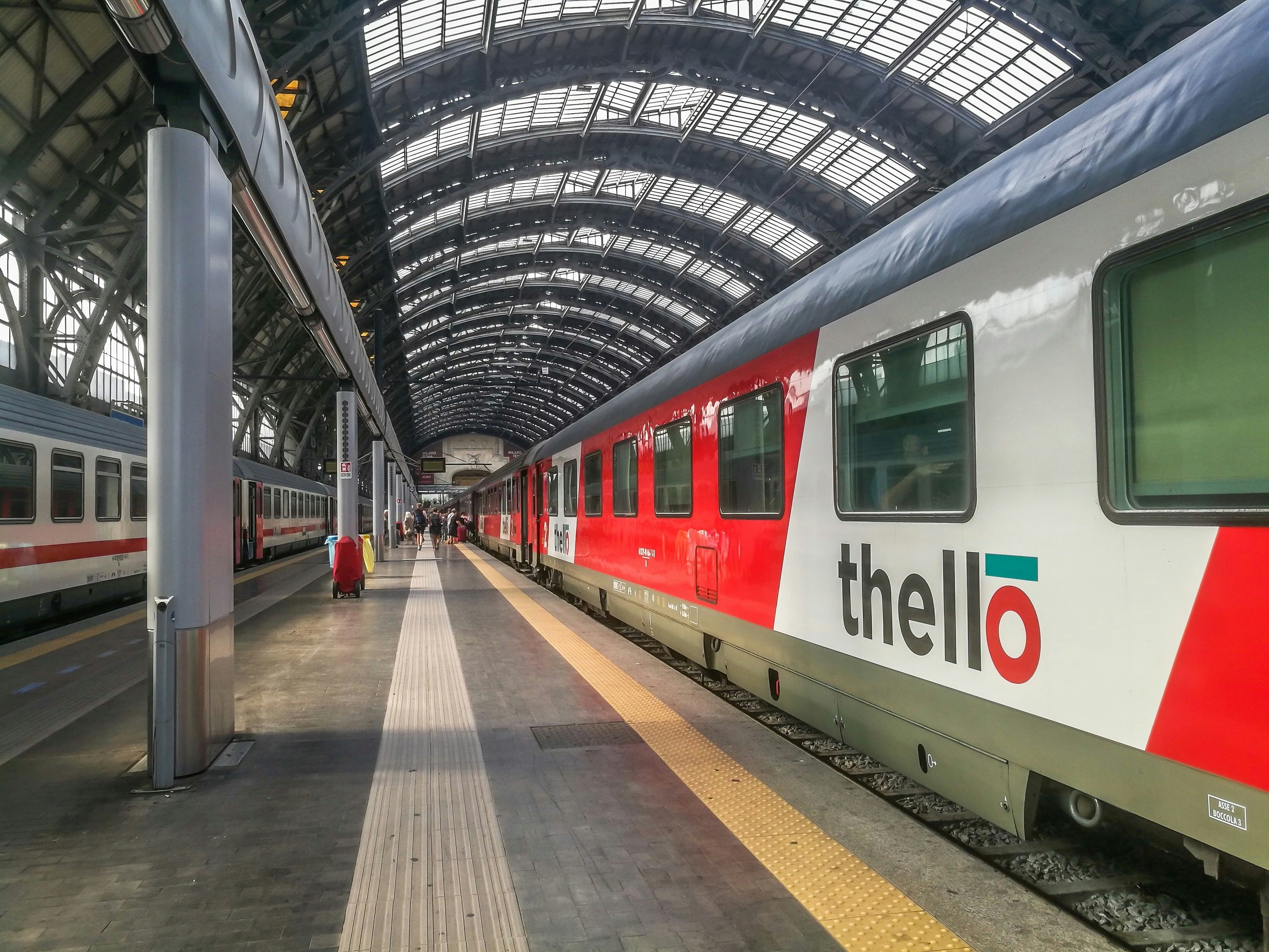 A red-and-white train with the word "Thello" on its side waits at a train station platform
