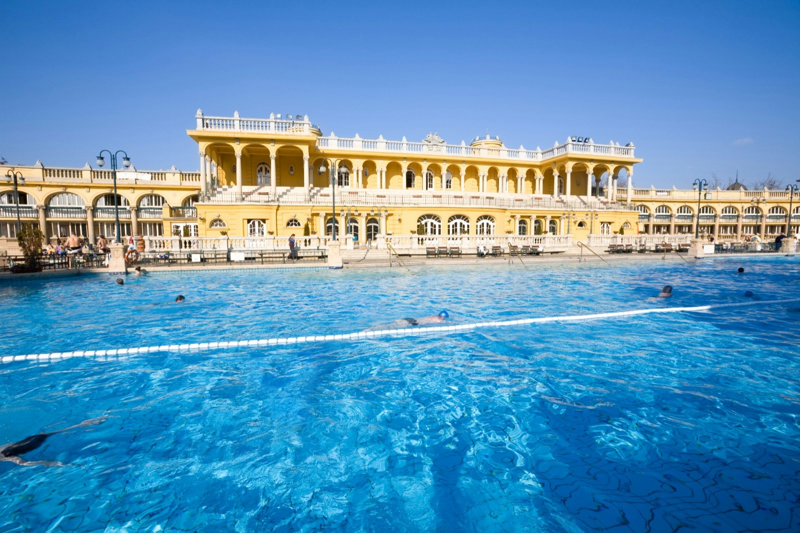 A clear blue swimming pool with an elaborate yellow building in the background