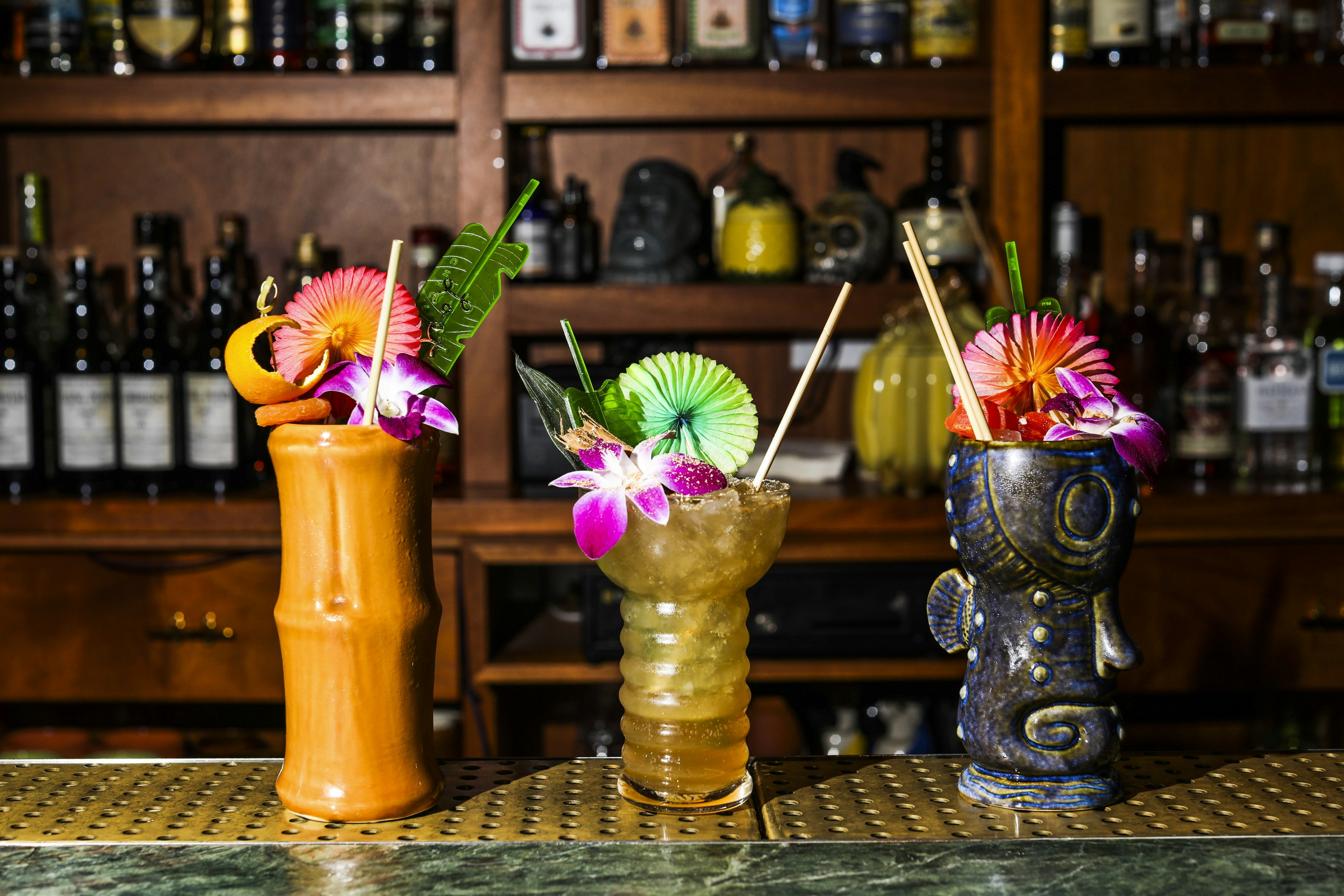 Three cocktails in colorful faux-Polynesian tiki mgus sit on the bar at Lost Lake in Chicago