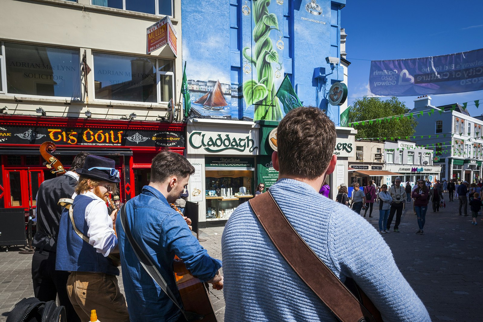 A group of musicians play Irish instruments in front of the red facade of Tig Cóilí. Galway, Ireland.