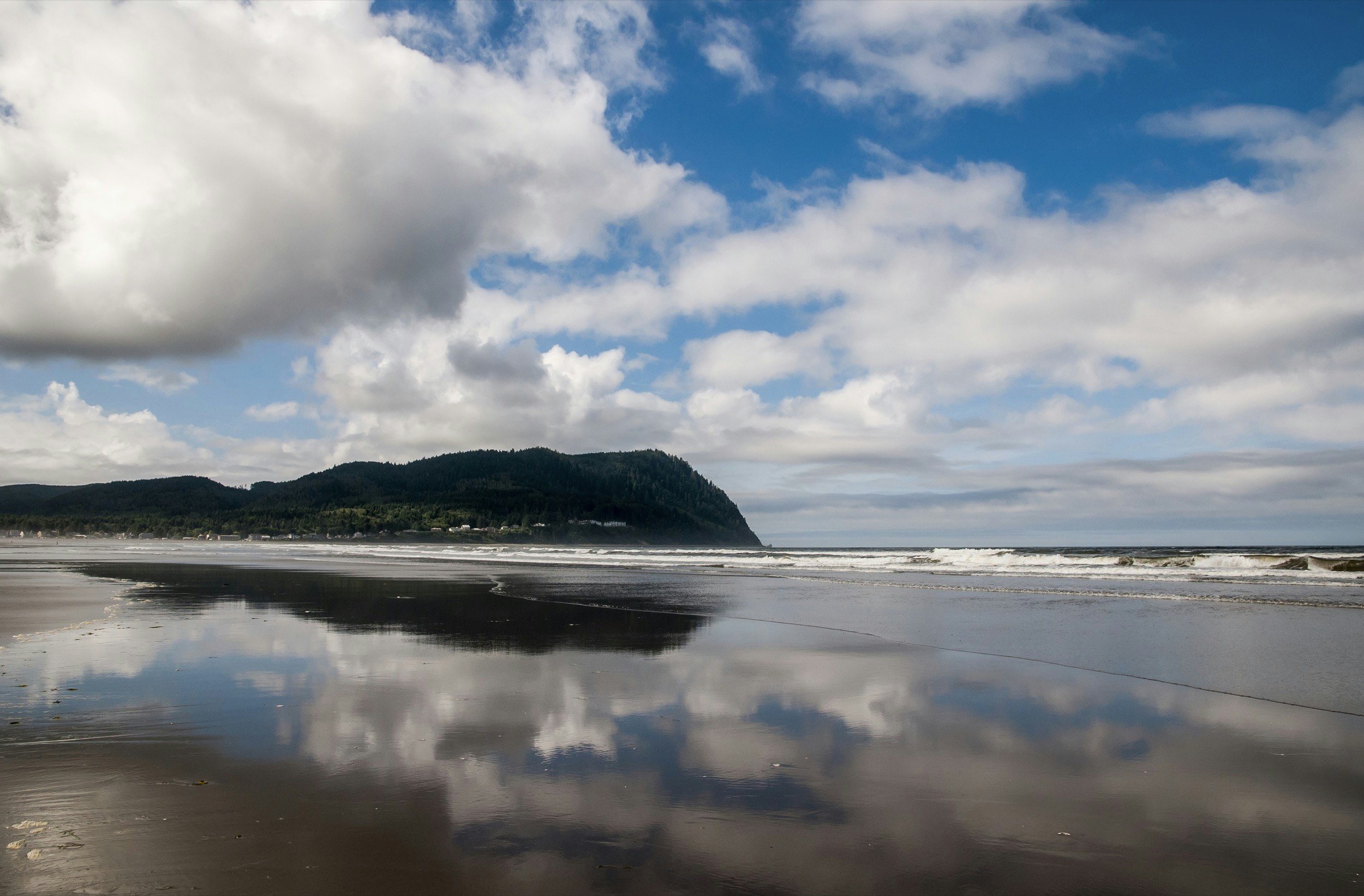 Tillamook Head is reflected in the water on a beach off the coast of Oregon