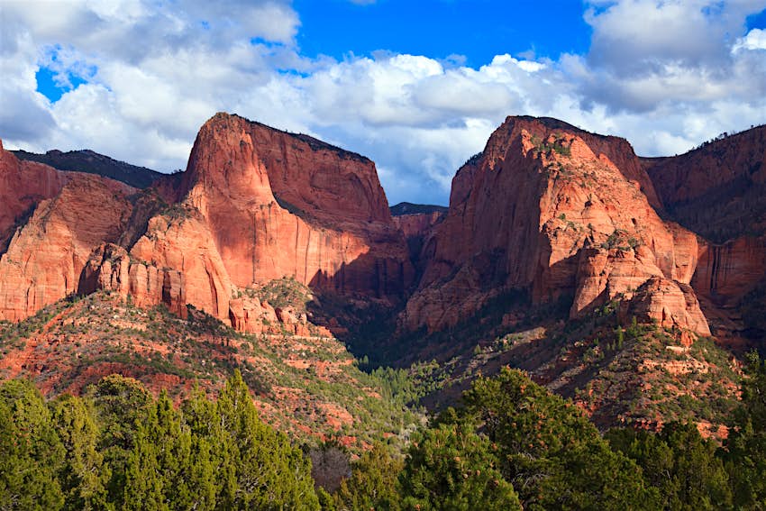 A red-rock mountain, with green trees below and blue skies above