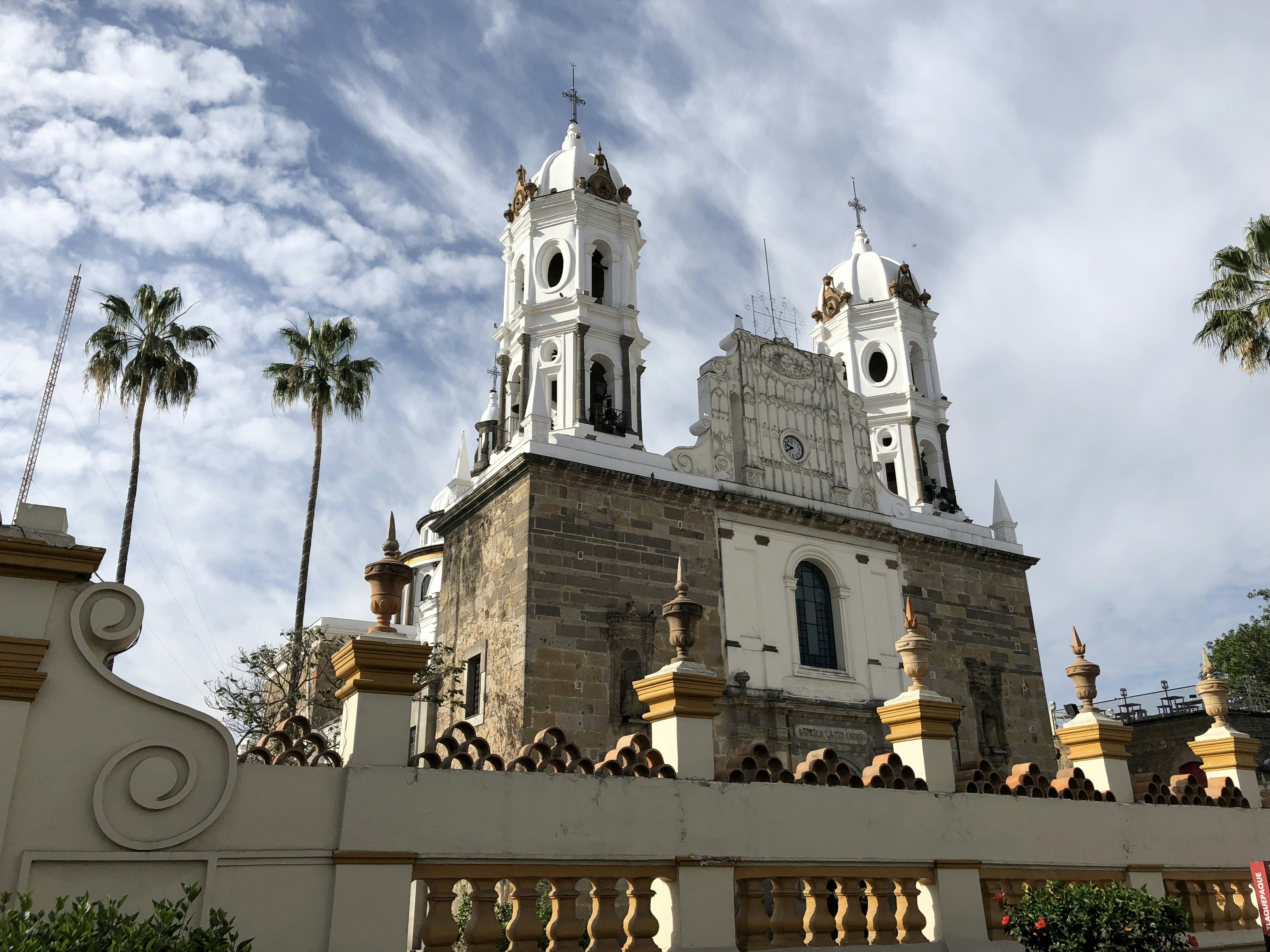 One of the imposing churches in Tlaquepaque, Mexico, with white domes, a stone facade and palm trees next to it.