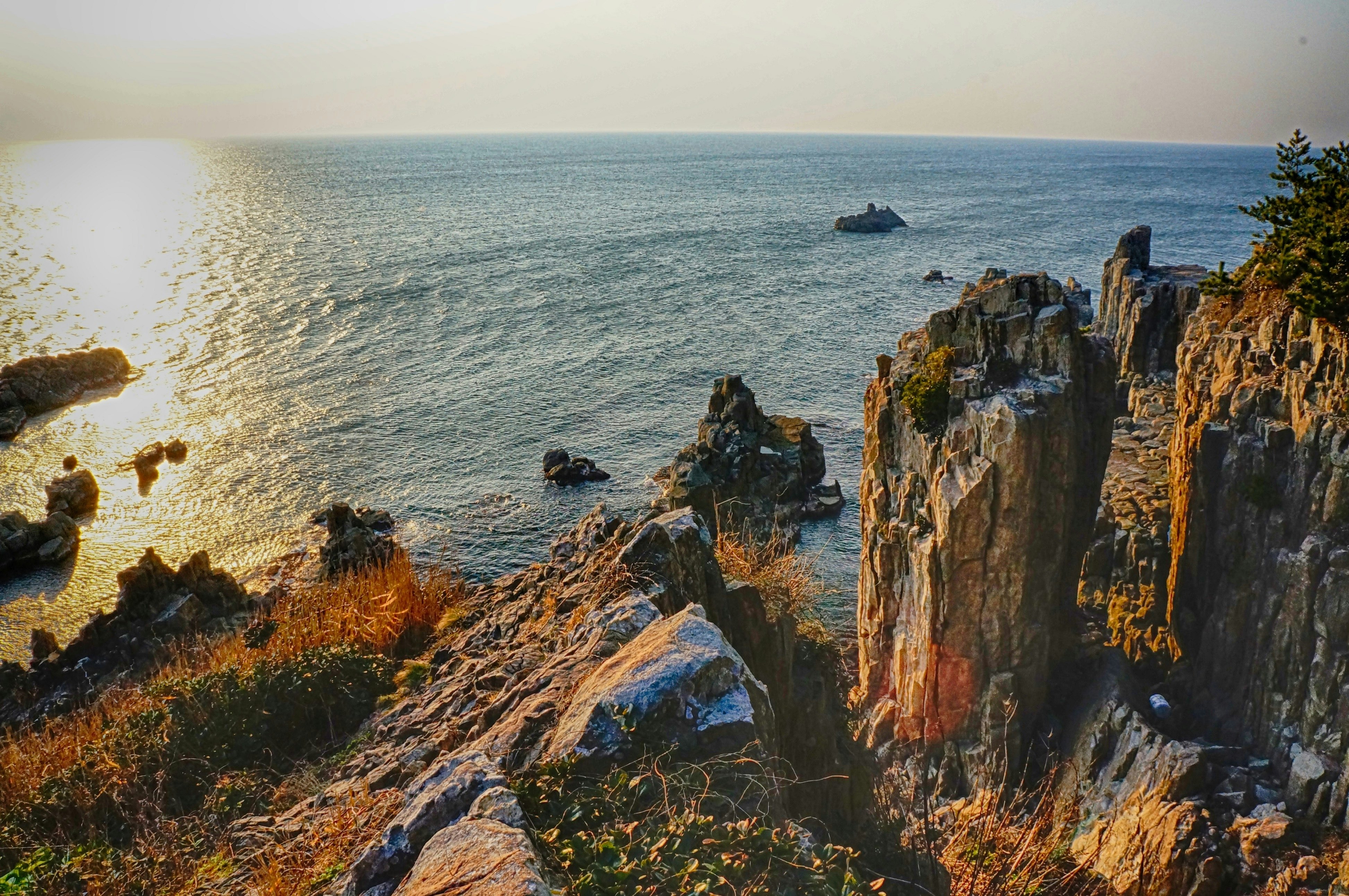 A coastal view looking out to sea at sunset. The rocks on the coast are jagged and some form pillar-like structures.