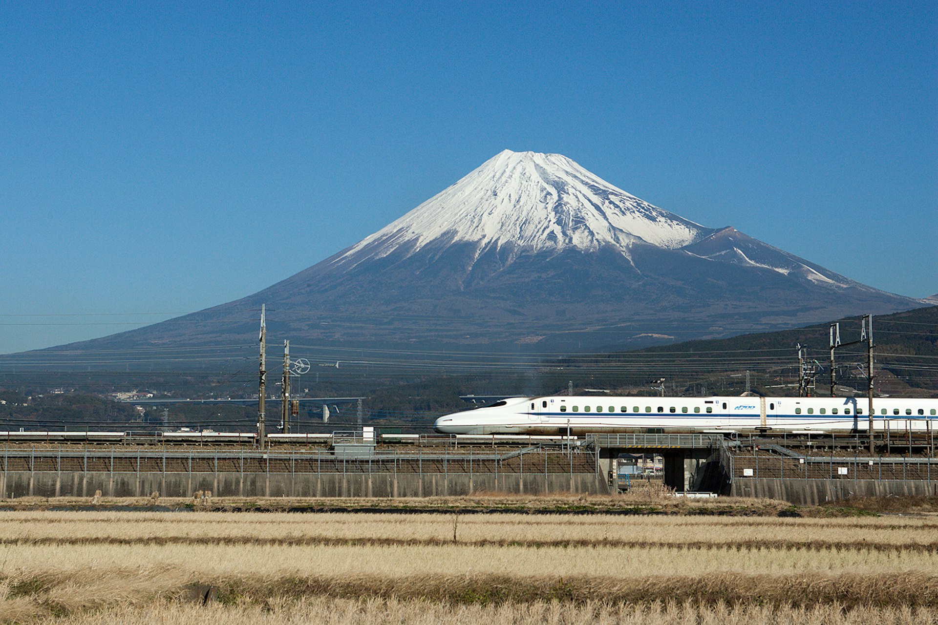 A bullet train in Japan passing snow-covered Mount Fuji with a blue-sky backdrop 